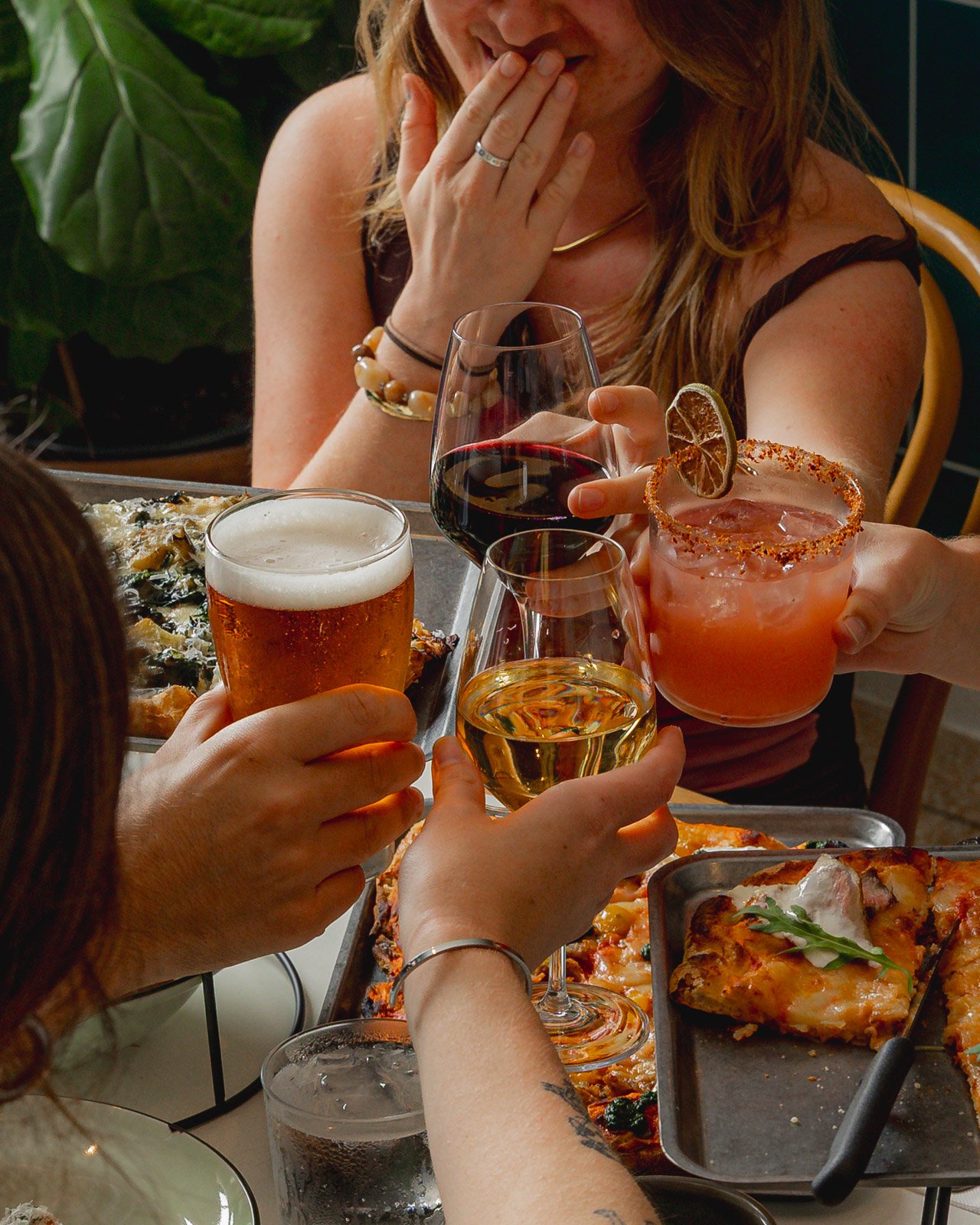 People holding various drinks around a table with pizza, celebrating and socializing.