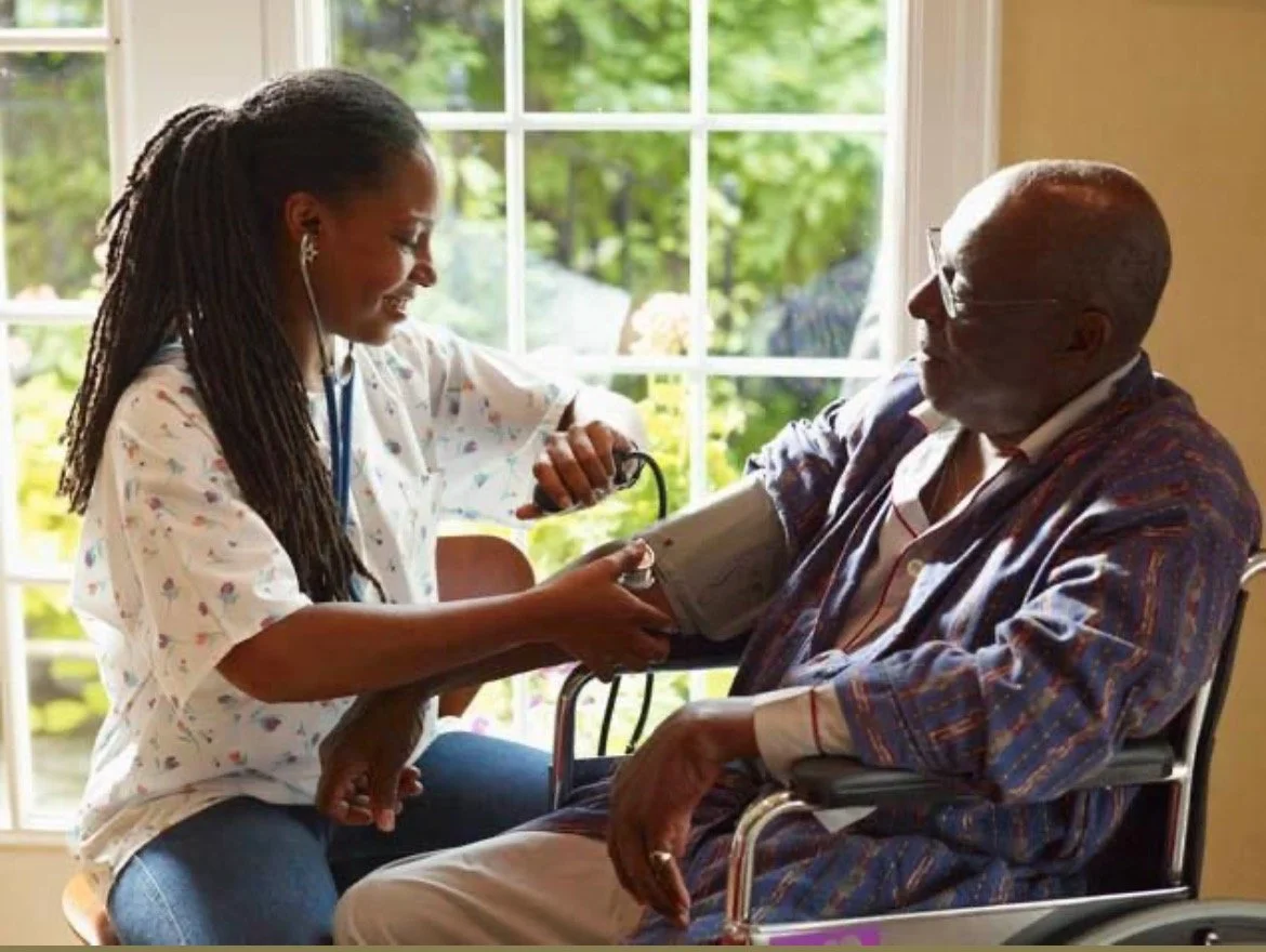 A young female healthcare worker measuring an elderly man's blood pressure with a cuff while he sits in a wheelchair by a window