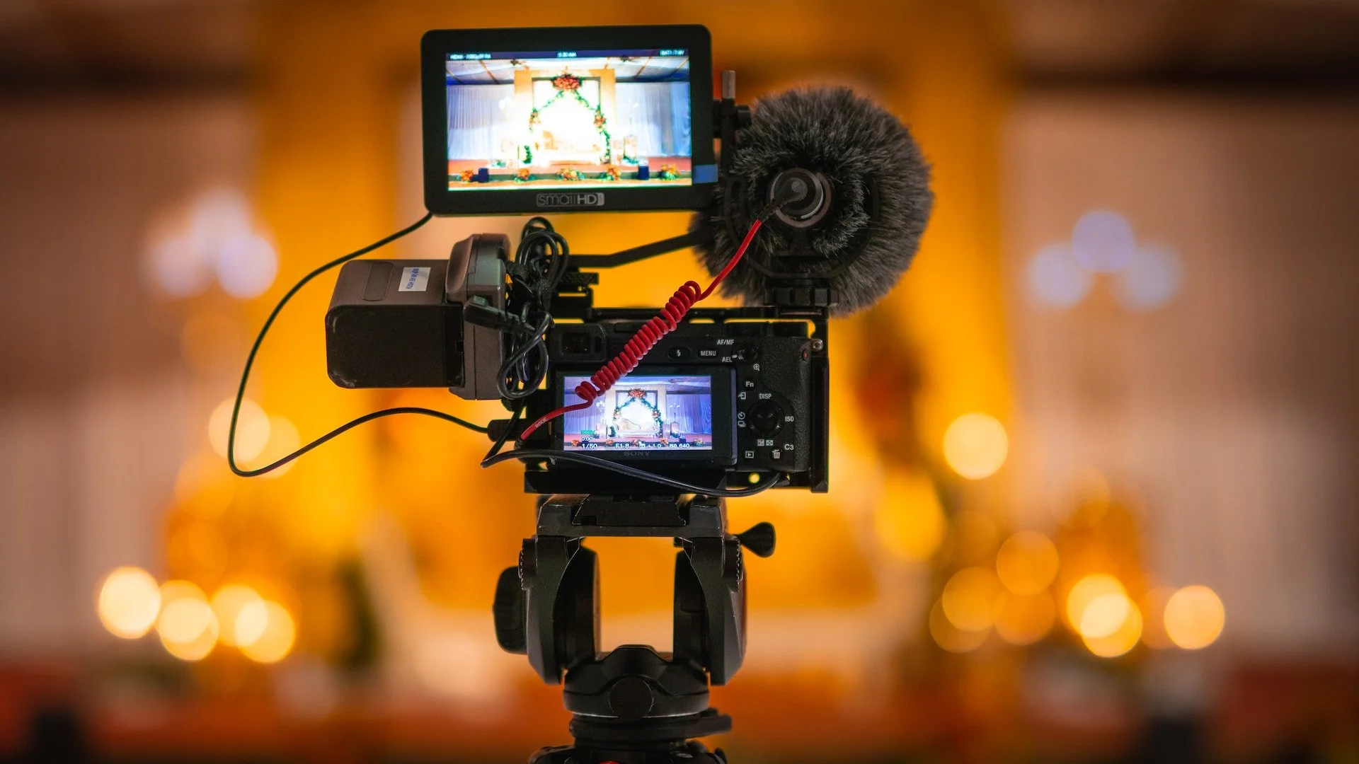 A professional video camera on a tripod records the interior of a church decorated for Christmas, with a nativity scene and holiday decorations in the background.