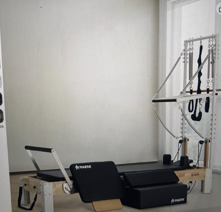 Pilates reformer machine and other Pilates equipment in a home studio with beige walls and a window with white curtains