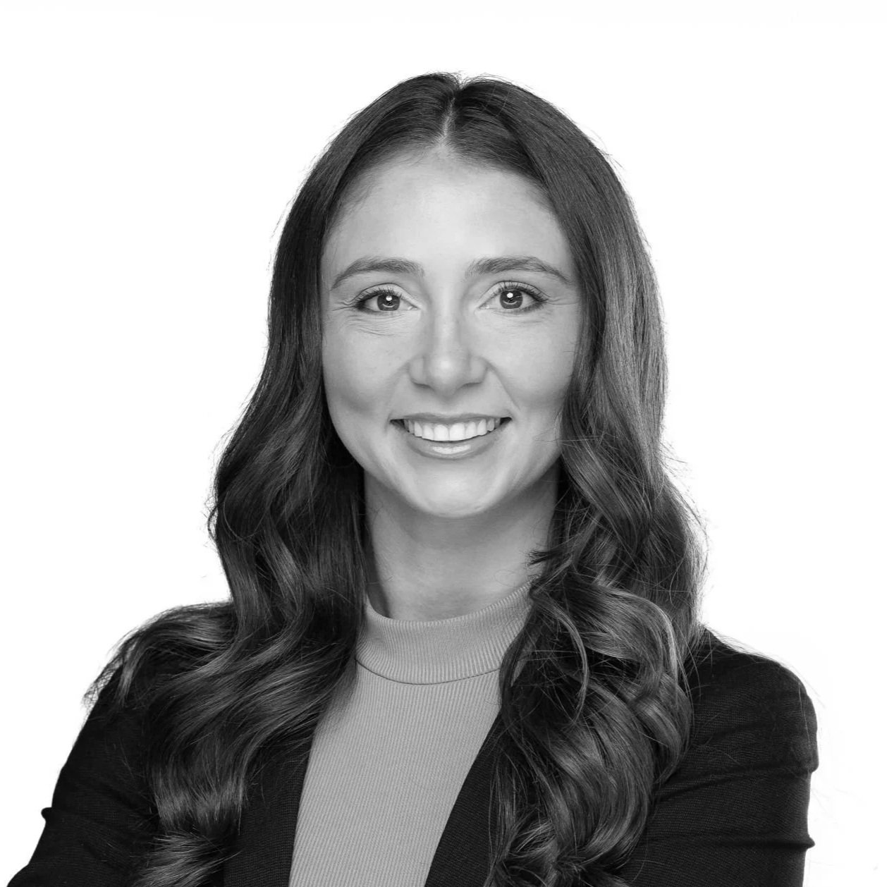 Black and white portrait of a woman with long wavy hair, smiling, wearing a blazer and a turtleneck top.