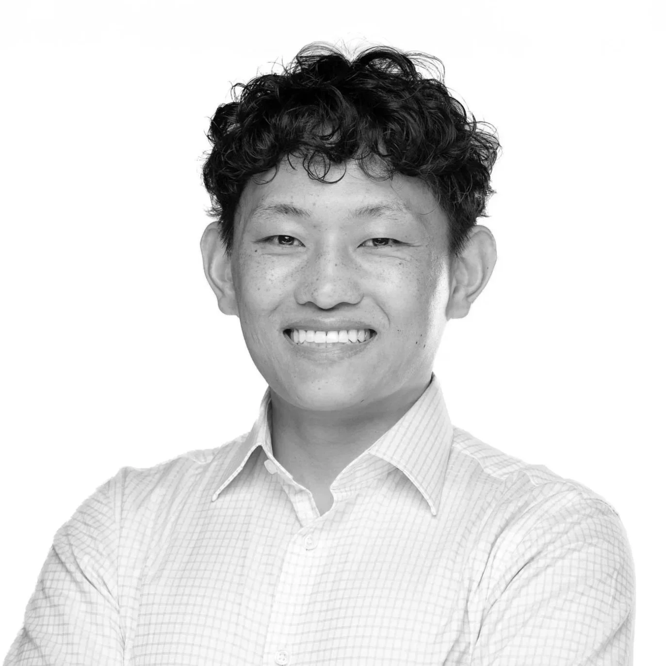 Black and white portrait of a smiling man with curly hair wearing a collared shirt