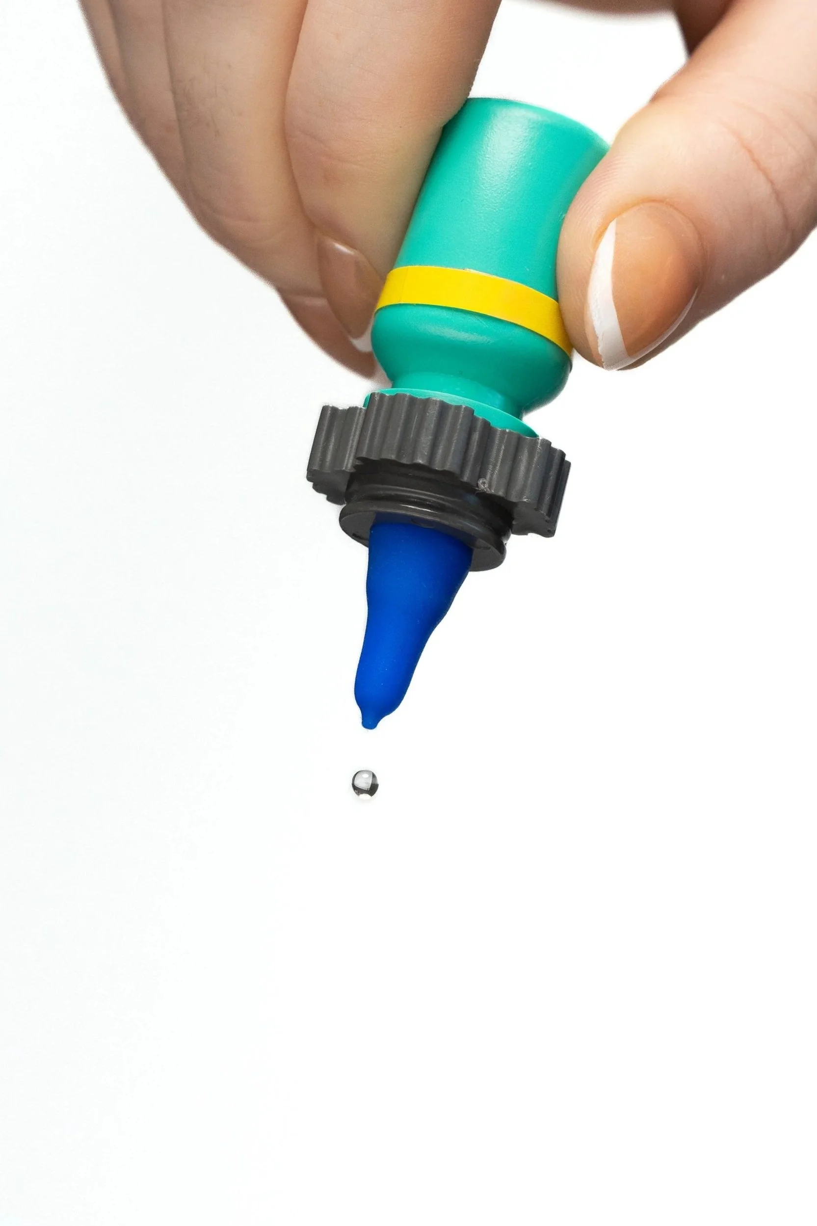 A person's hand holding a Nanodropper Adaptor with an eyedrop falling from the tip.