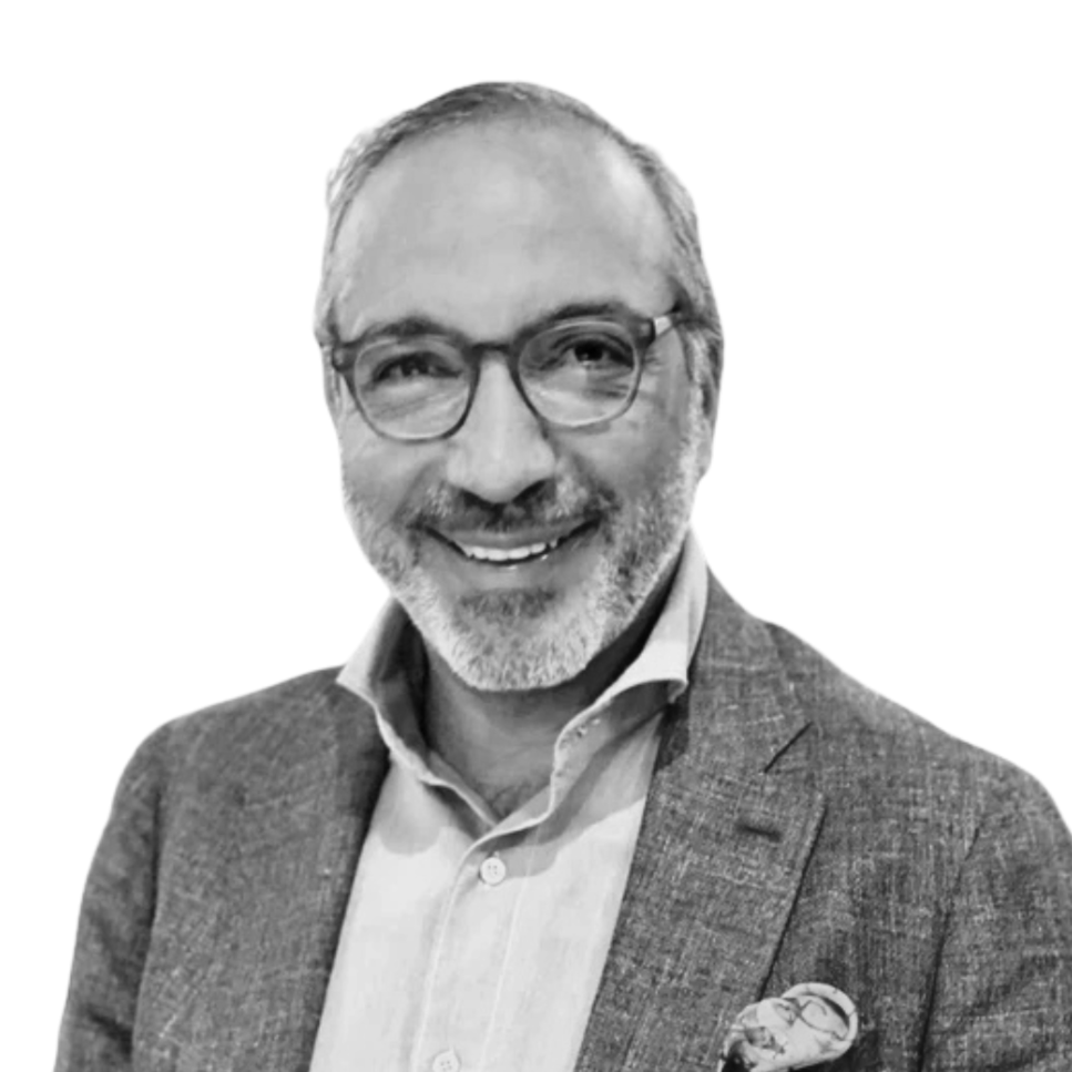 Black and white photo of a smiling middle-aged man with glasses, beard, wearing a suit jacket and shirt, against a plain background.