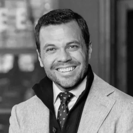A smiling man in a suit and tie, posed for a portrait in grayscale.