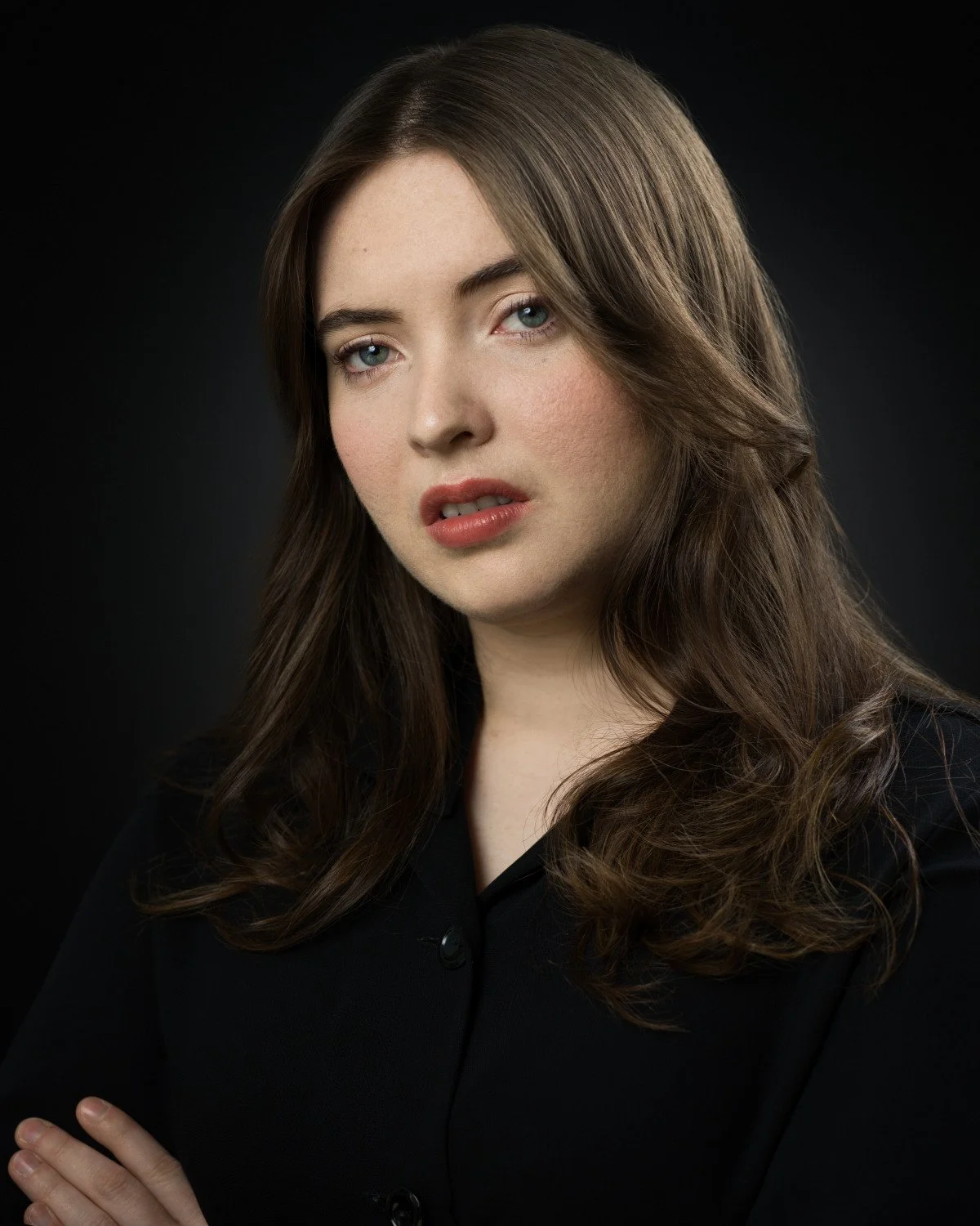Dramatic headshot of Skyela Jones with a reactive, intense expression and crossed arms. Her direct gaze and parted lips suggest a character in a moment of urgent discovery or intellectual challenge, perfect for high-stakes dramatic & procedural roles