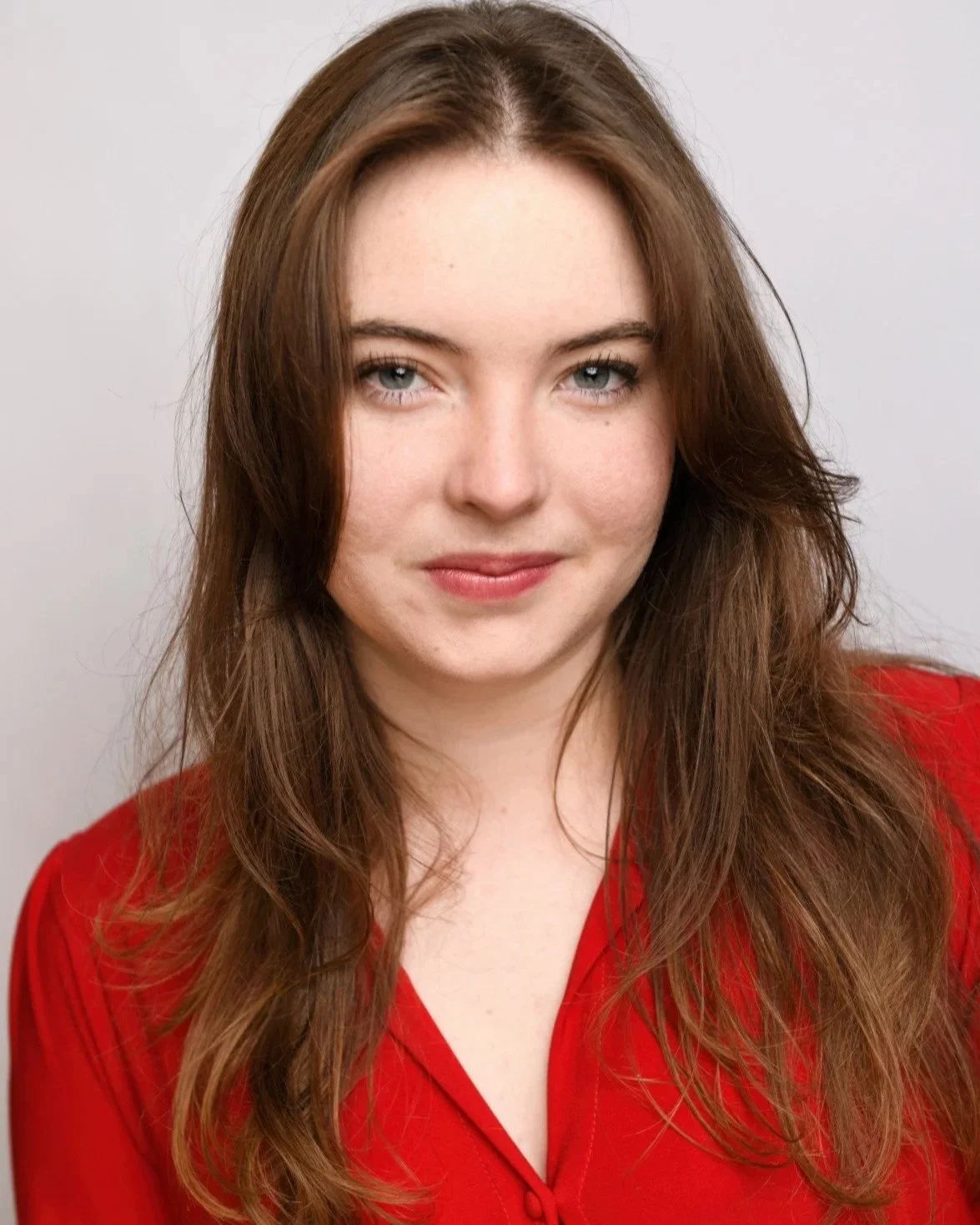 Commercial Headshot of Skyela Jones in a vibrant red top with a slight, playful head tilt. Her engaging smile and direct, intelligent gaze convey a charismatic and resourceful presence, ideal for clever contemporary protagonists.