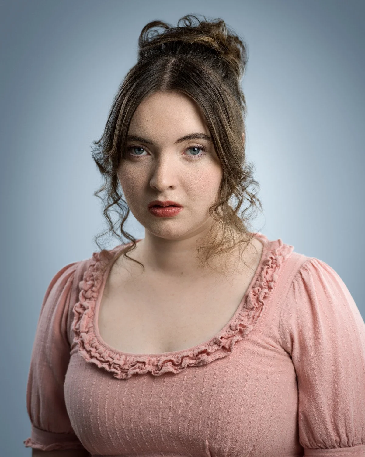 A vulnerable, evocative headshot of Skyela Jones. Her slightly parted lips and searching gaze in a soft pink period dress suggest a character in a moment of emotional discovery or quiet shock, ideal for sensitive dramatic roles.