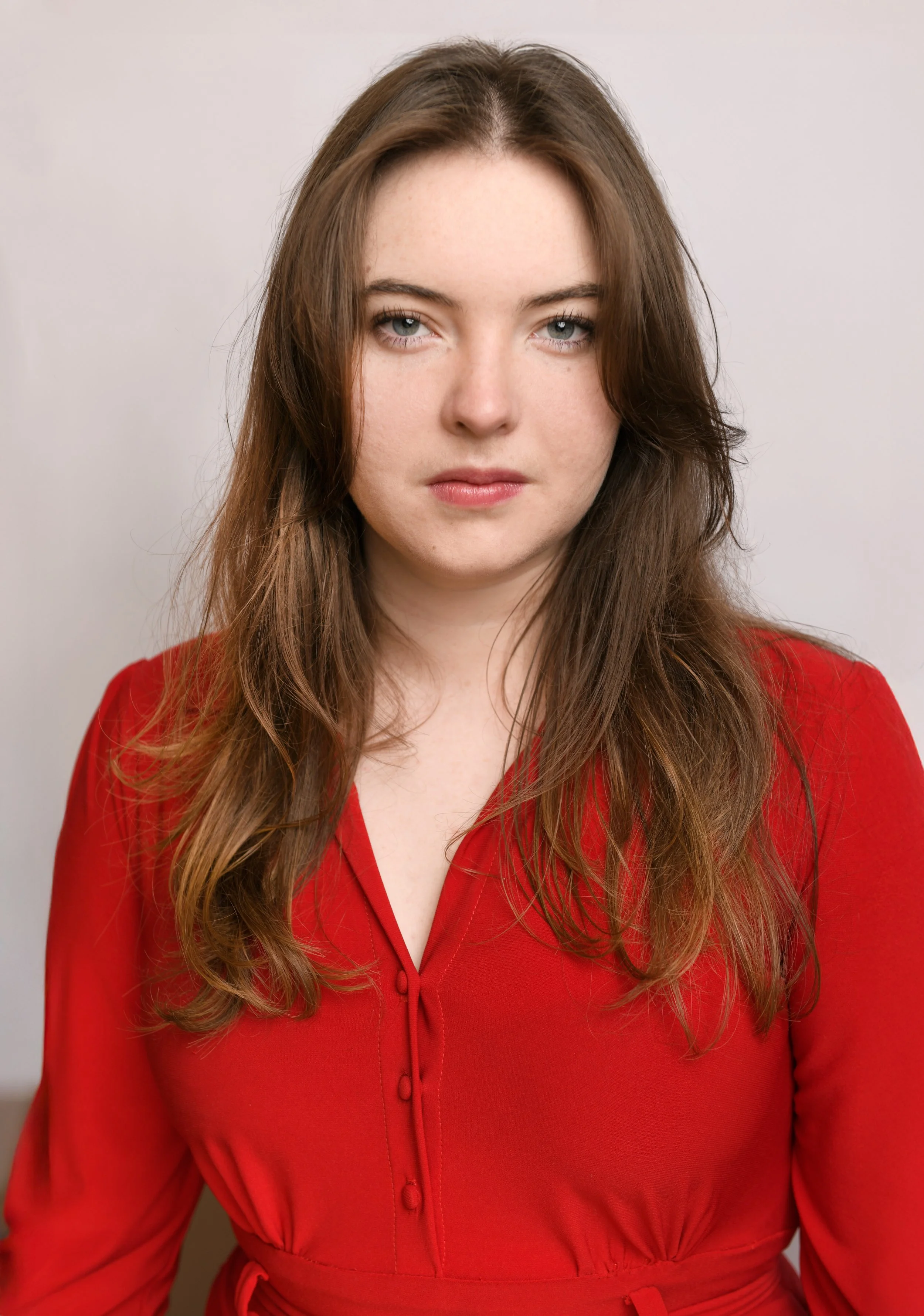 Modern theatrical headshot of Skyela Jones in a vibrant red dress, featuring a steady, unwavering gaze and a resolute expression. Her direct and authentic presence suggests a strong-willed, contemporary character, ideal for leading dramatic roles and