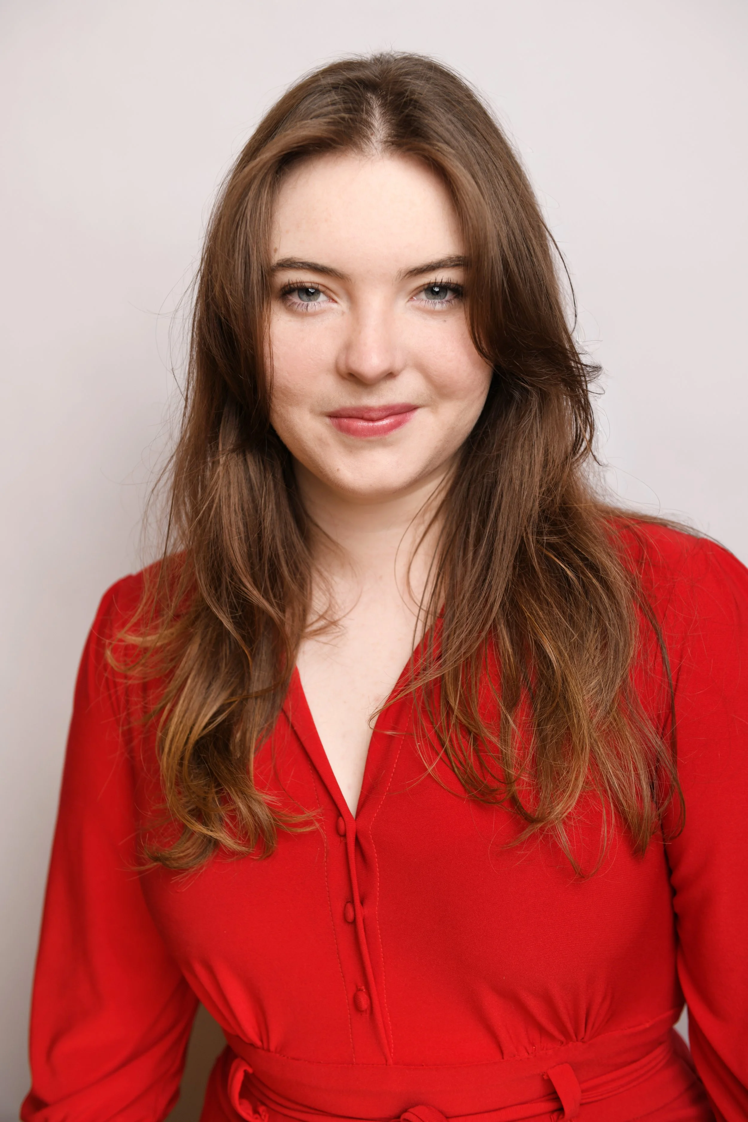 A warm and approachable commercial headshot of Skyela Jones in a vibrant red dress. Her soft smile and direct, engaging gaze convey a relatable and grounded authenticity, ideal for contemporary leading roles and professional commercial projects.