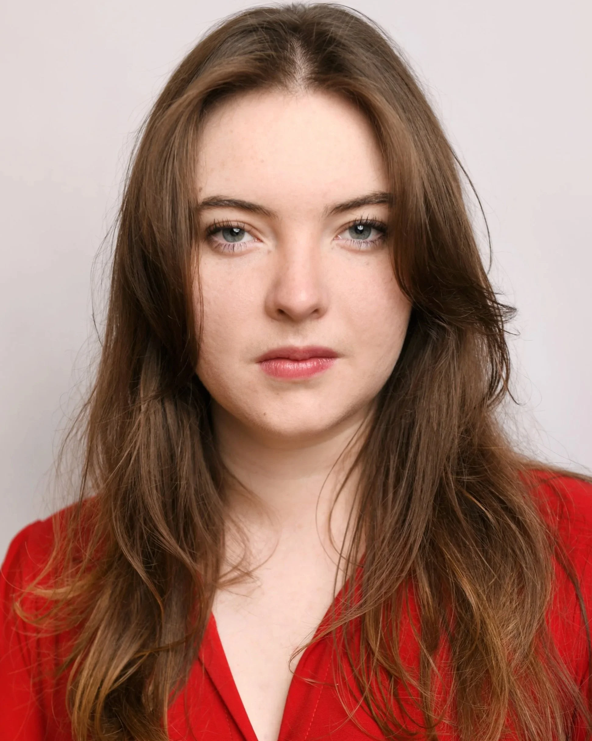 Modern theatrical headshot of Skyela Jones in a vibrant red top with hair down and natural. Her steady, unblinking gaze conveys a raw, grounded authenticity and strong-willed presence, perfect for contemporary drama and outspoken leading roles.