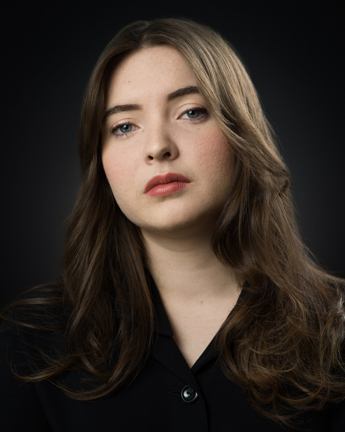 Theatrical headshot of Skyela Jones with a steady, enigmatic gaze and a neutral, authoritative expression. Her presence is sharp and observant, suggesting a character of high intelligence and focused intent, perfect for dramatic and procedural roles.