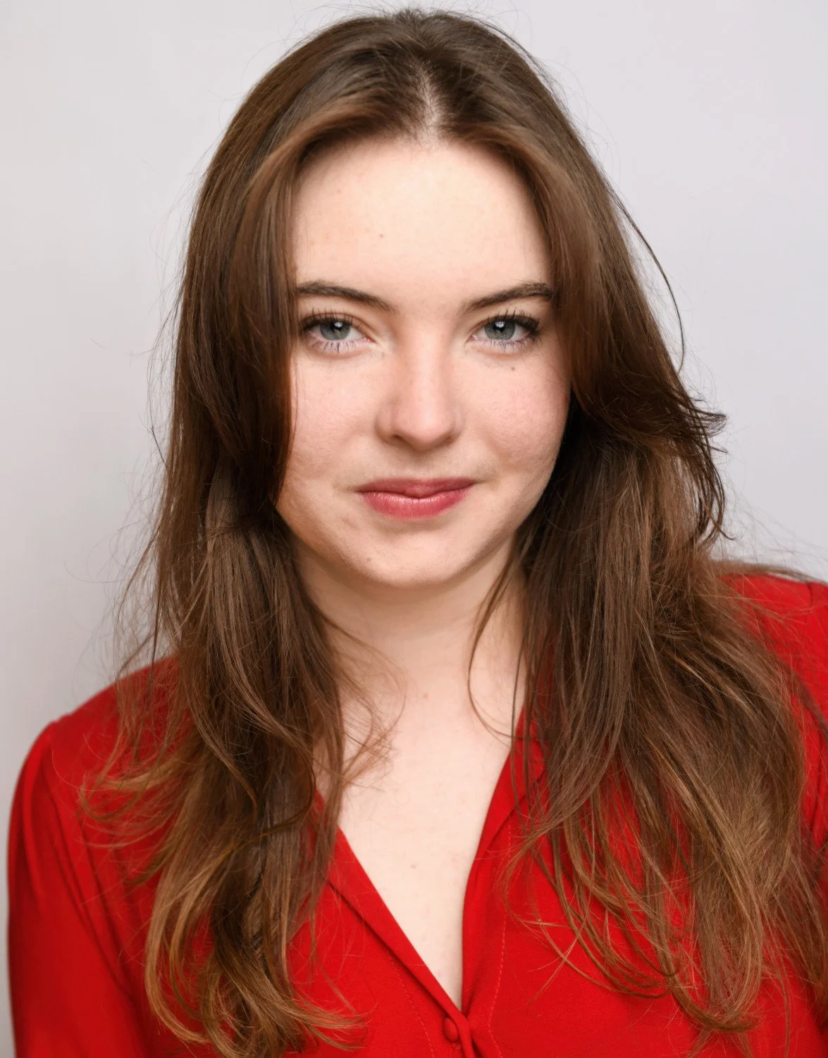 Commercial headshot of Skyela Jones in a vibrant red top with a slight, playful head tilt. Her engaging smile and direct, intelligent gaze convey a charismatic and resourceful presence, ideal for spirited modern leads and clever contemporary protagon