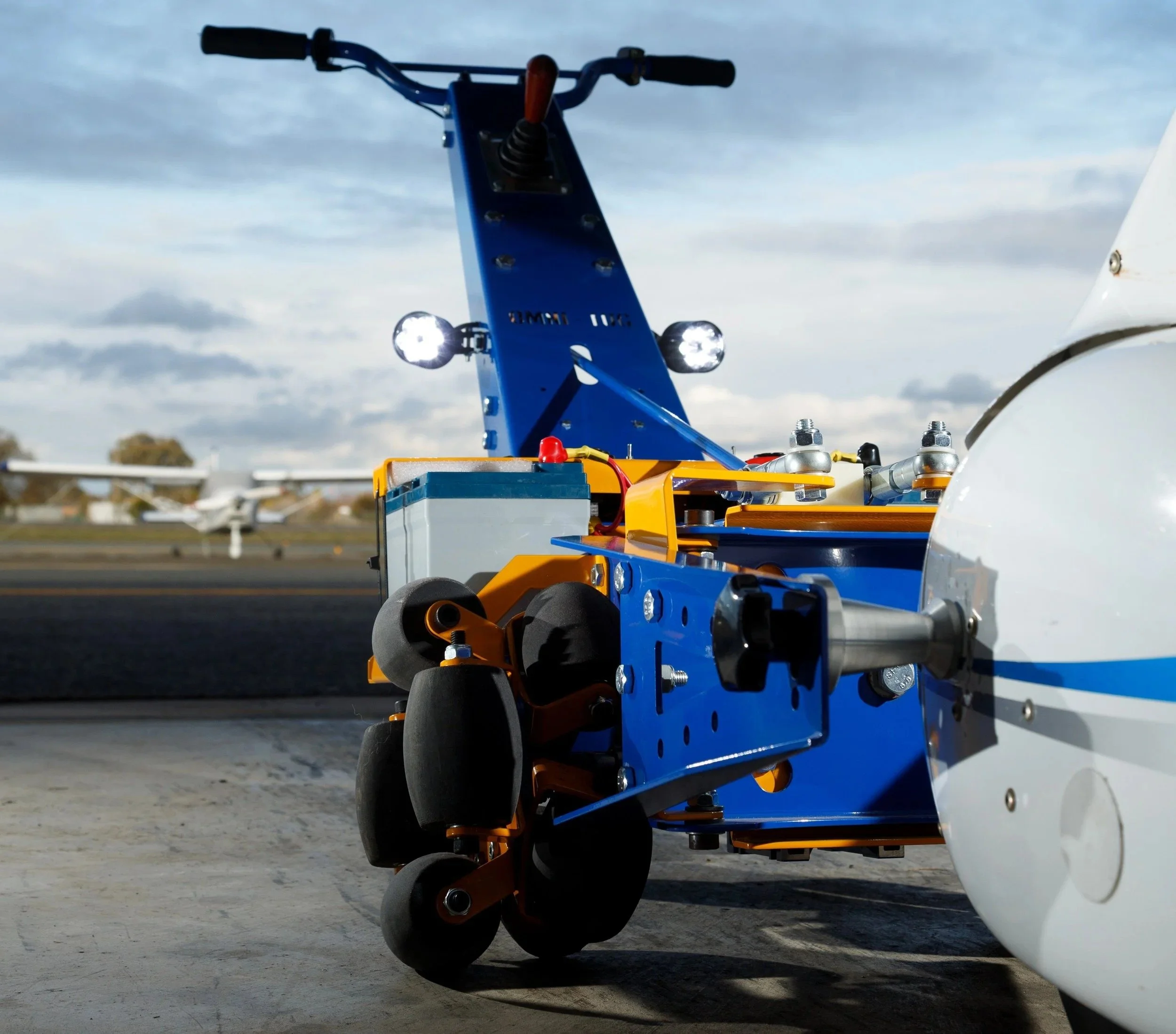 Close-up view of a remote-controlled drone with wheels, sensors, and LED lights, positioned on a tarmac against a cloudy sky background.