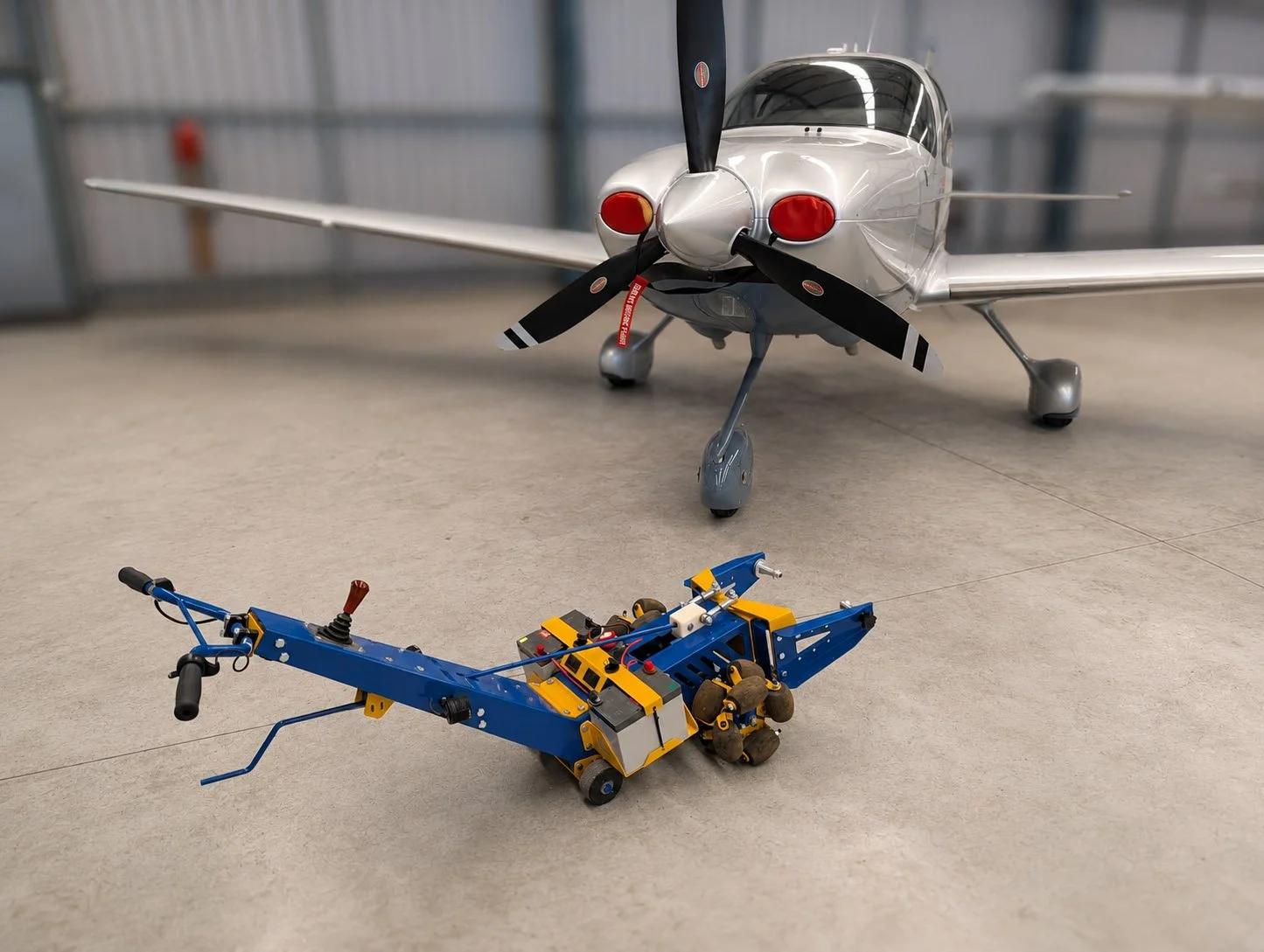 A small aircraft and a robotic vehicle on a concrete floor inside a hangar or industrial building