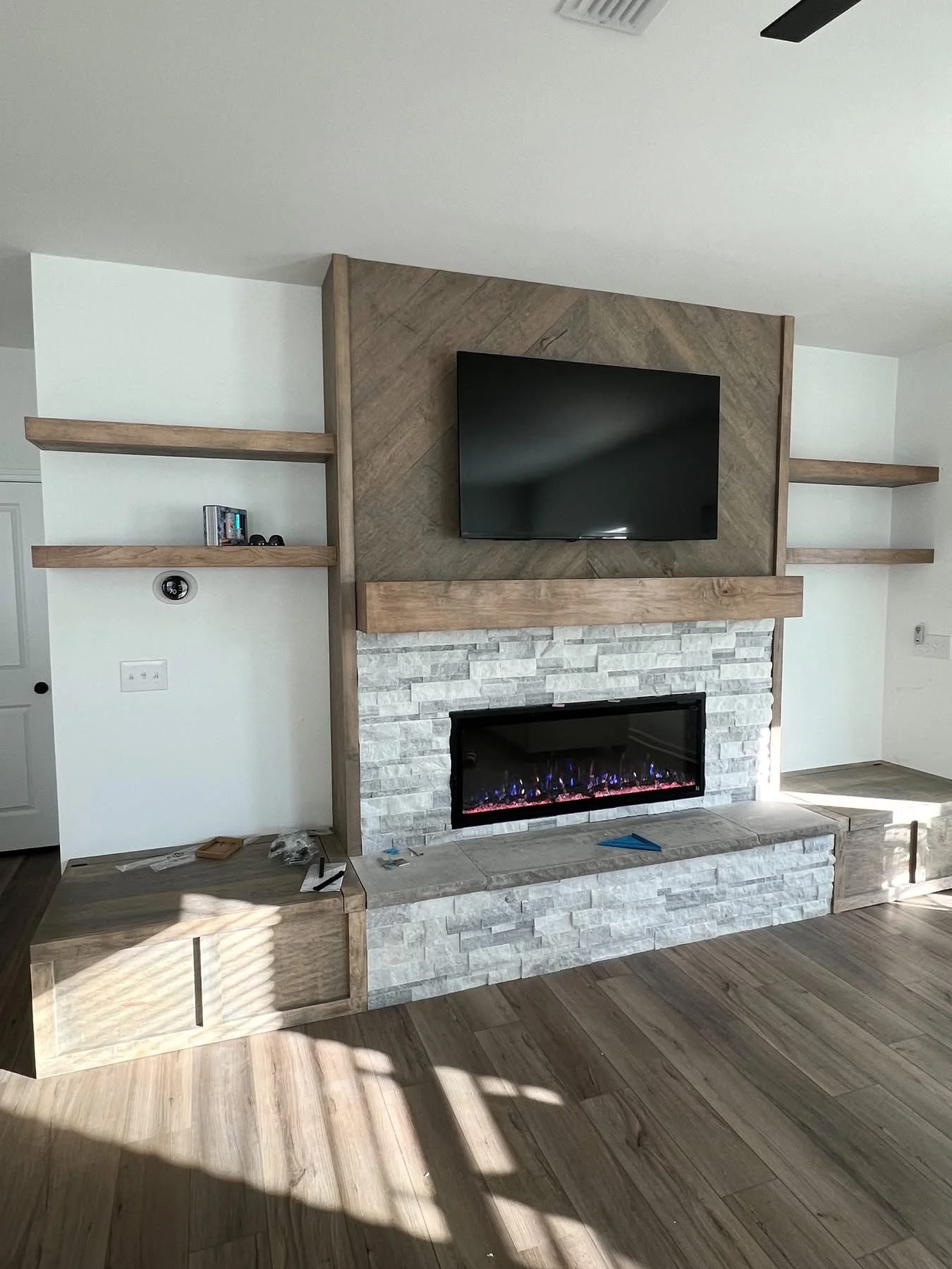 Living room fireplace with mounted flat screen TV, wooden mantel, stone surround, and built-in shelves on either side.