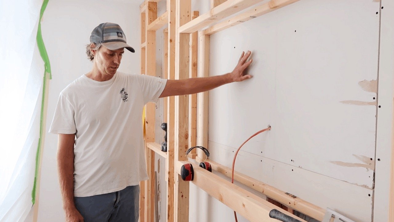 Man wearing a cap and t-shirt working on a wall frame in construction site.