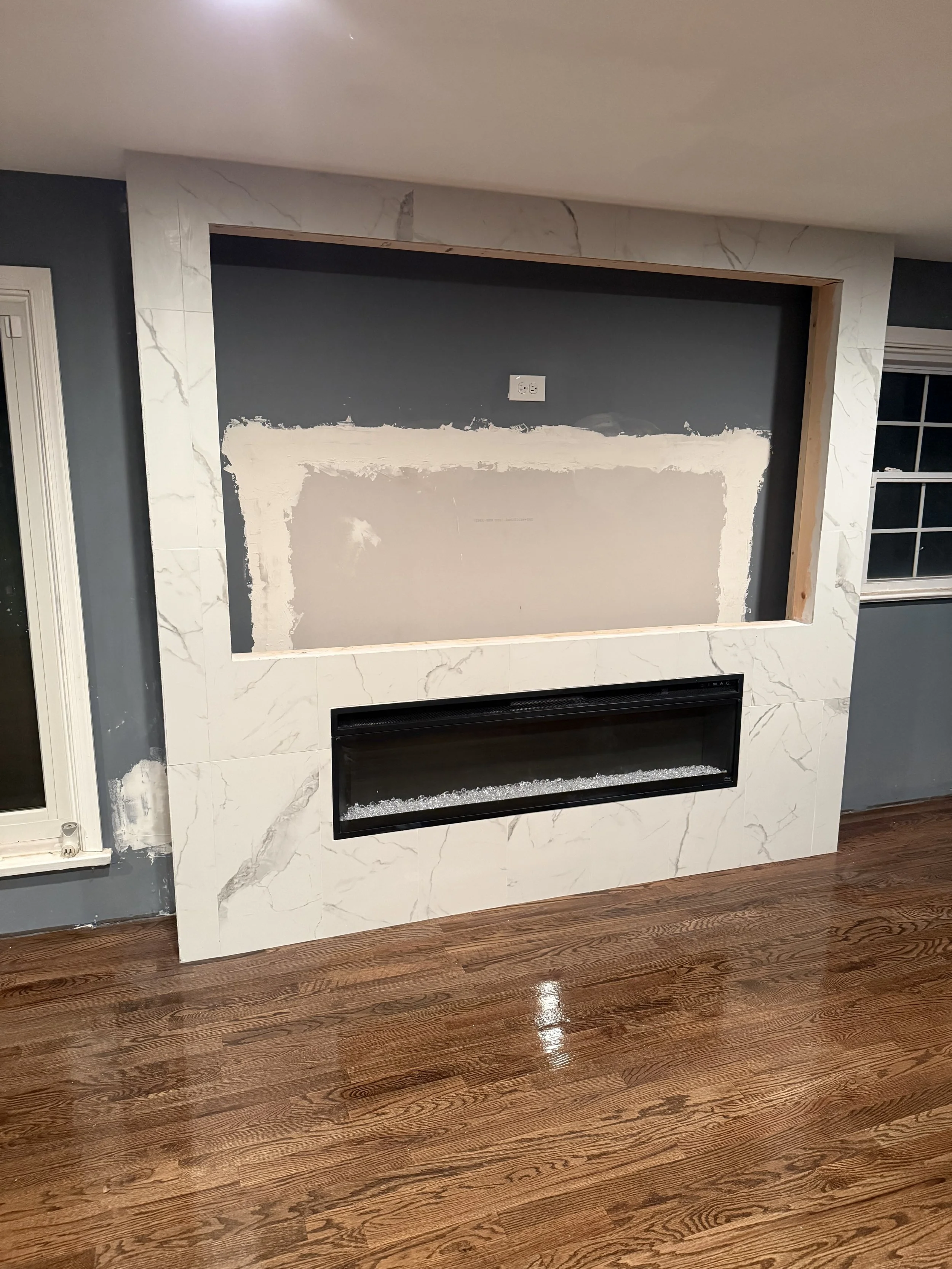 Living room fireplace with a marble surround, open wall space above, and hardwood floor.