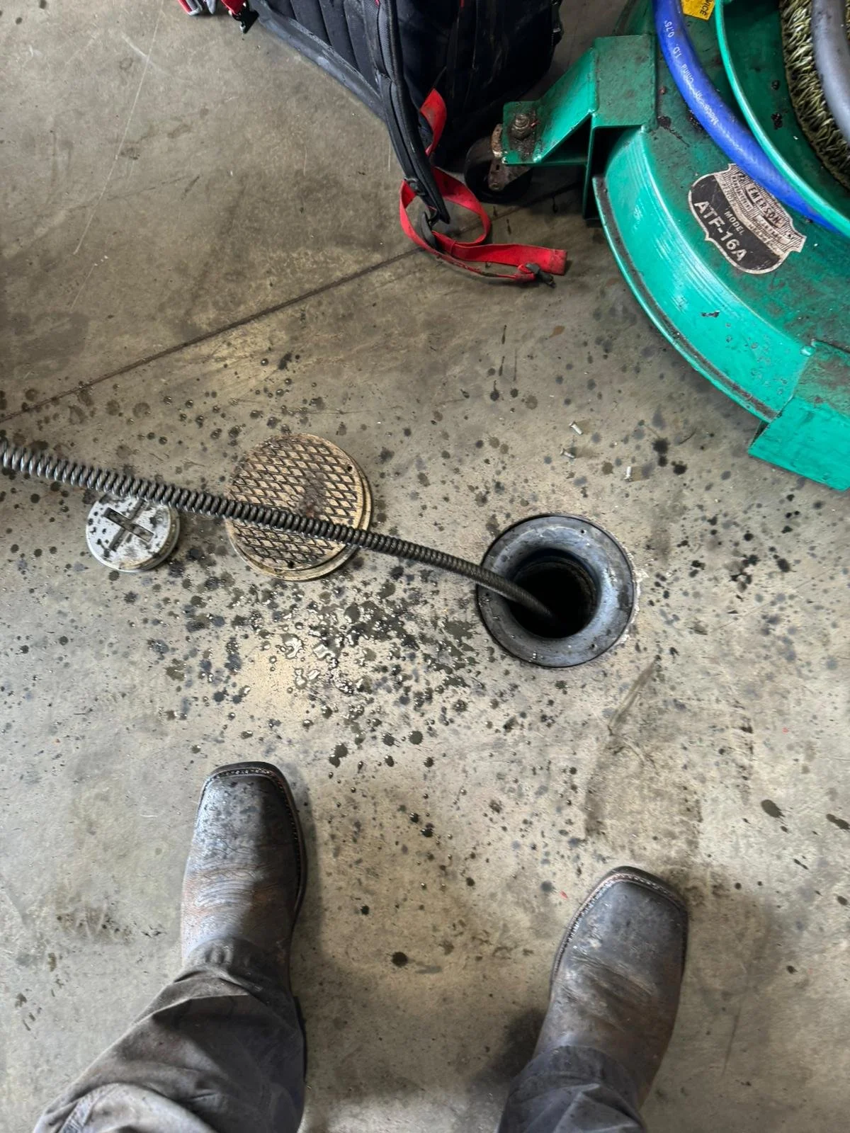 View of an industrial work environment with a drain snake in a floor drain, dirty boots, and industrial equipment.