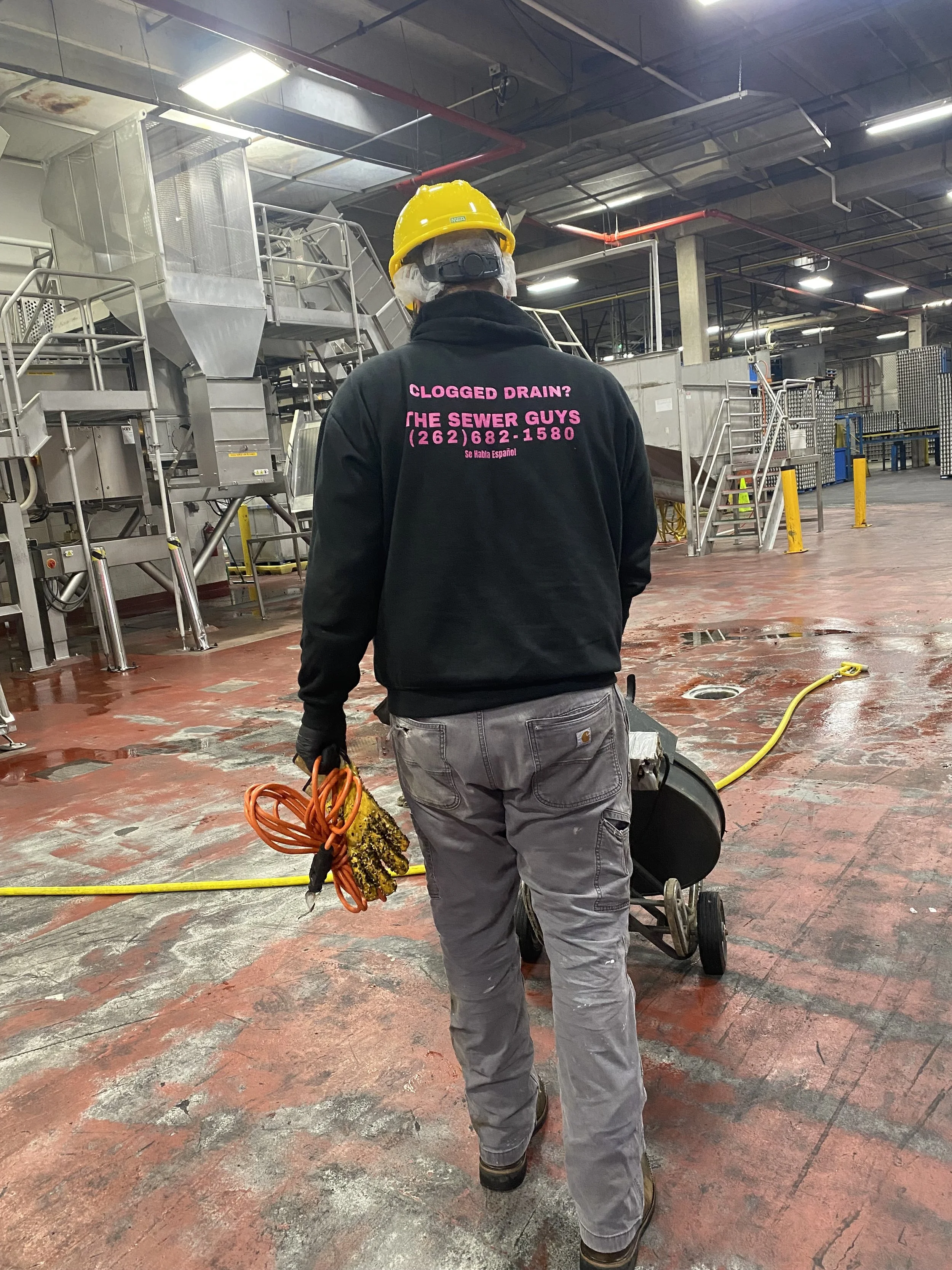 Worker in safety gear with drain cleaning equipment in industrial setting.
