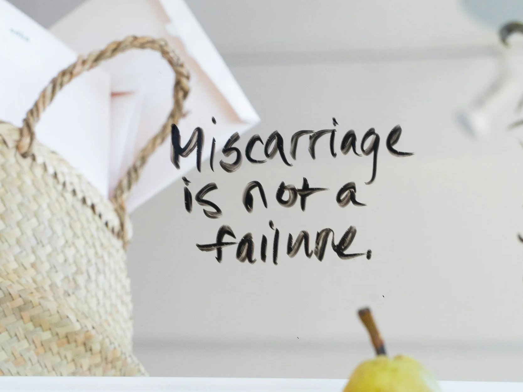 Mirror that reads "miscarriage is not a failure" with a basket and fruit in background