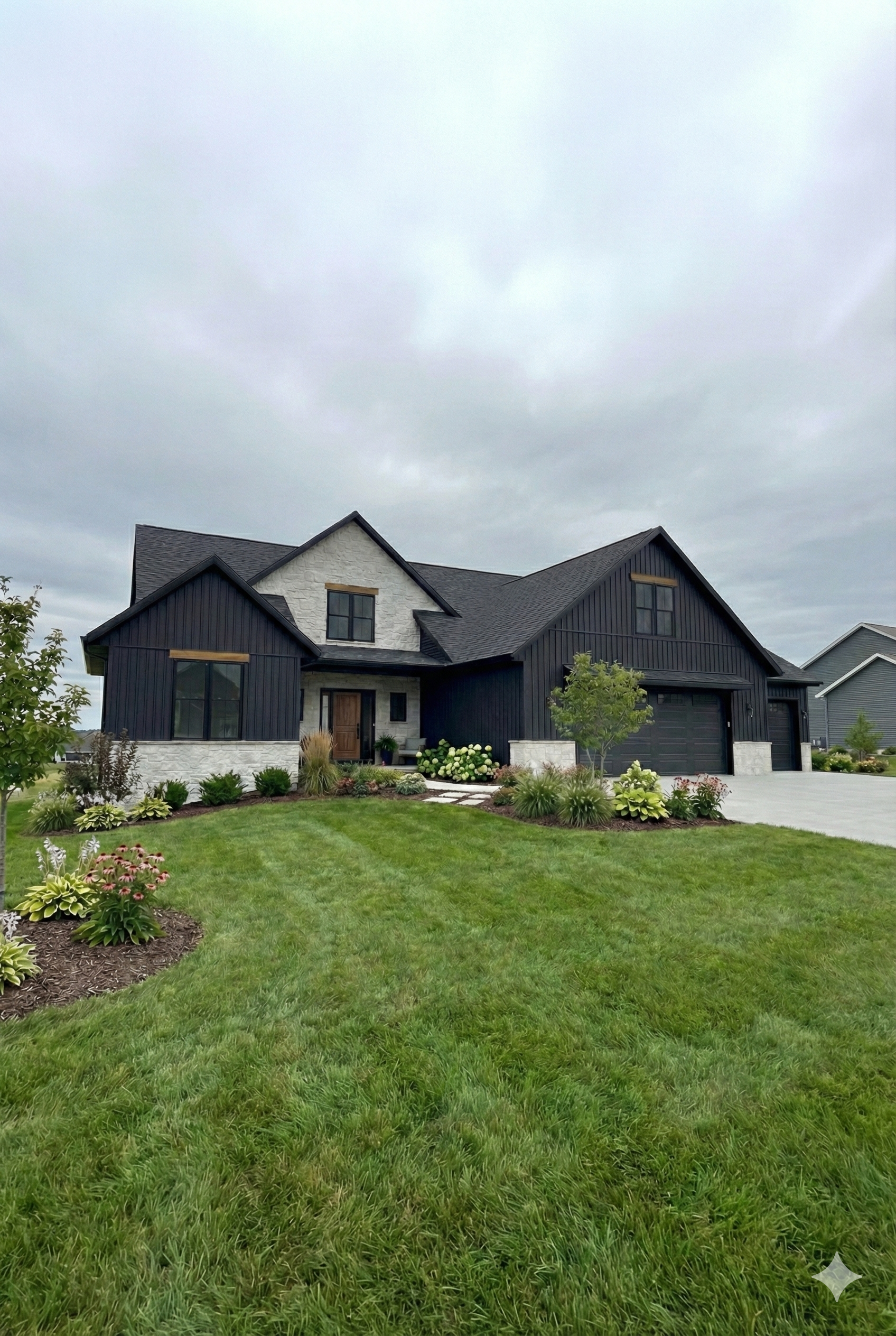 A modern two-story house with black and white exterior, a well-maintained lawn, landscaped garden, and an overcast sky.