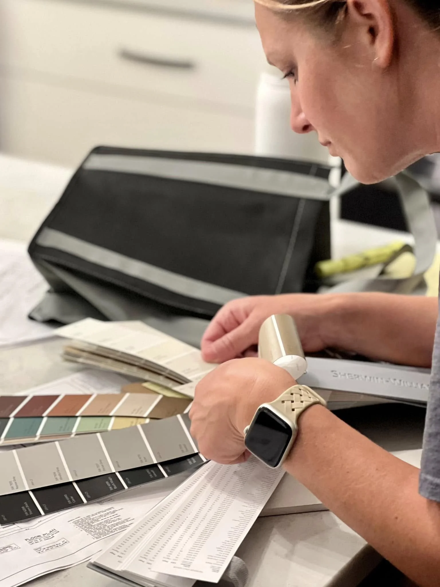 A woman examining a paint color fan deck and swatch samples at a table in a home improvement setting.