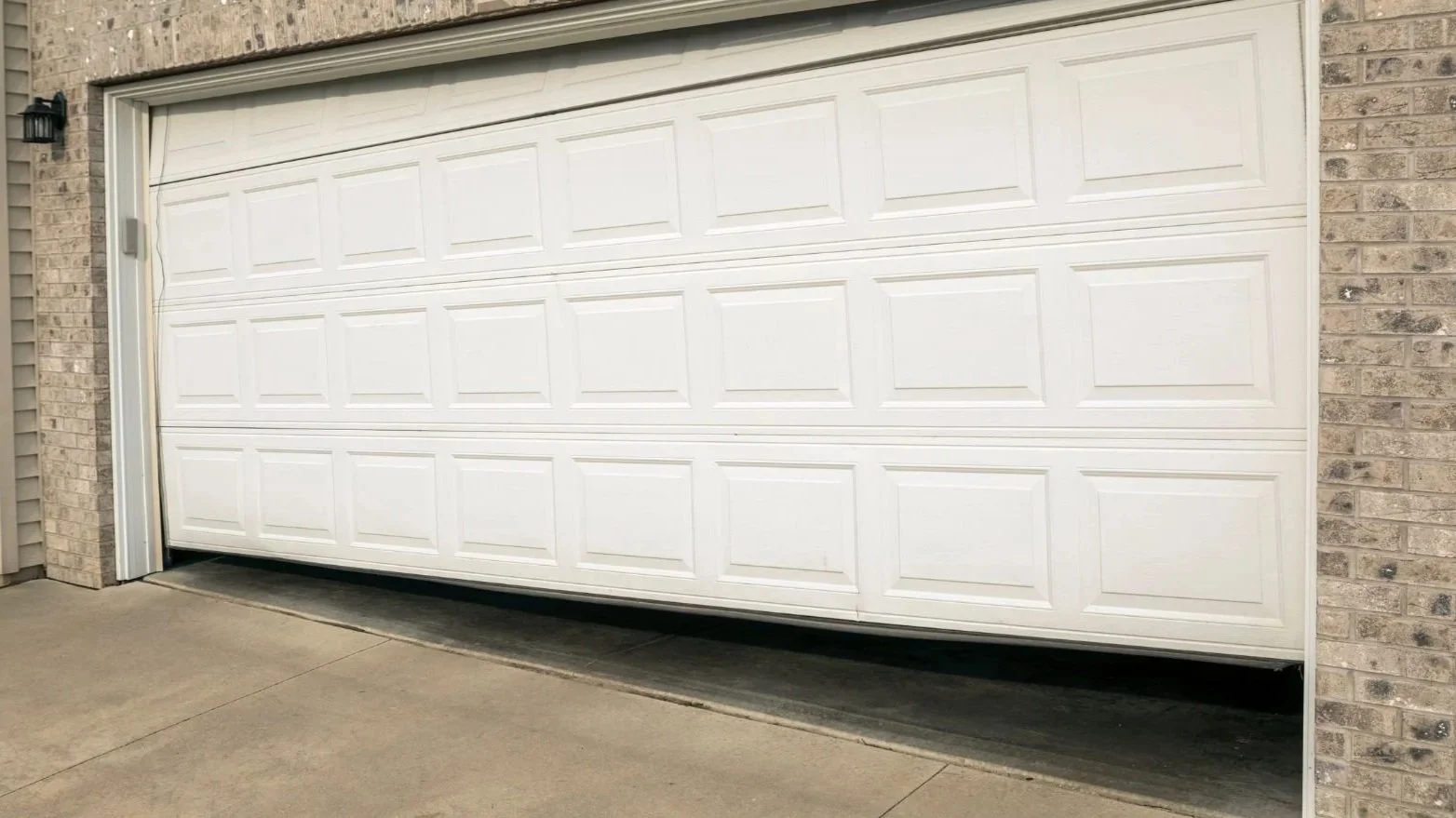 White sectional garage door partially open with brick exterior walls on both sides and concrete driveway.