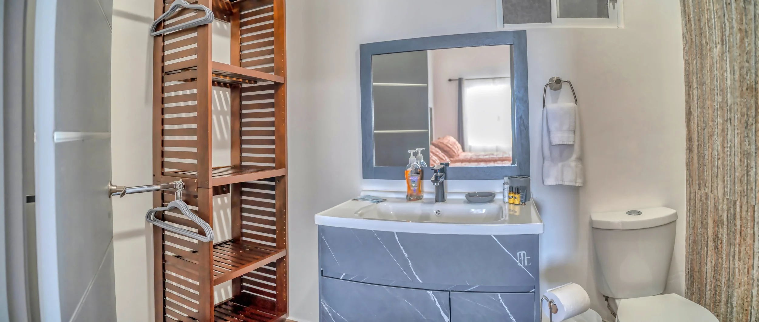 Baño moderno con espejo, lavabo, toallas colgadas y estantería de madera