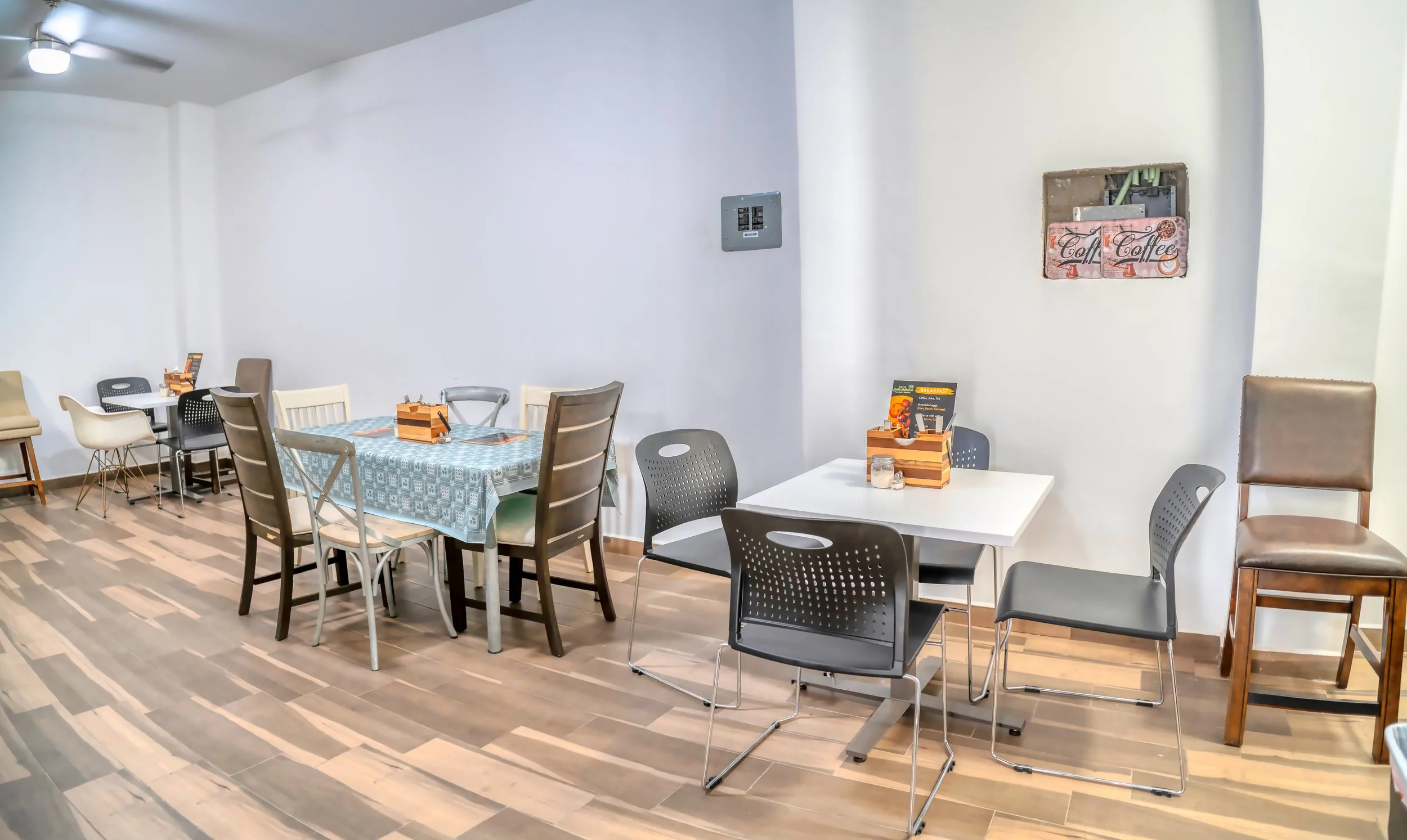 Mesas y sillas en un restaurante o cafetería, algunas con manteles y menús, en un ambiente luminiso y sencillo.