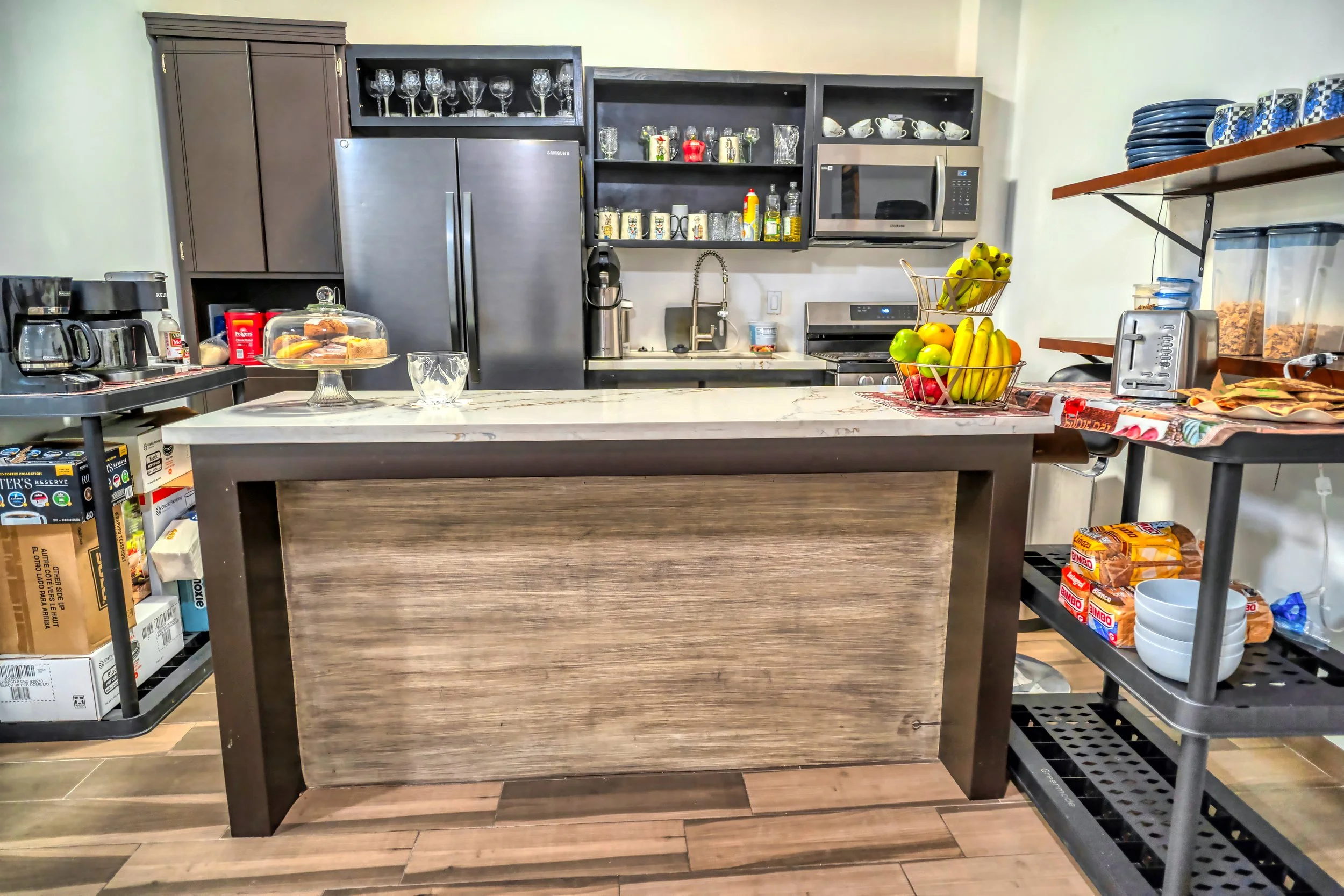 Una cocina moderna con estanterías abiertas, electrodomésticos en acero inoxidable y una mesa con frutas y pan.