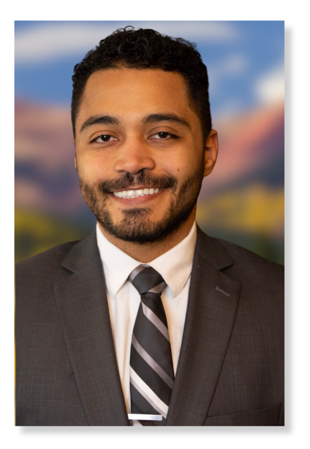 Portrait of a smiling man in a business suit with a blurred outdoor background.