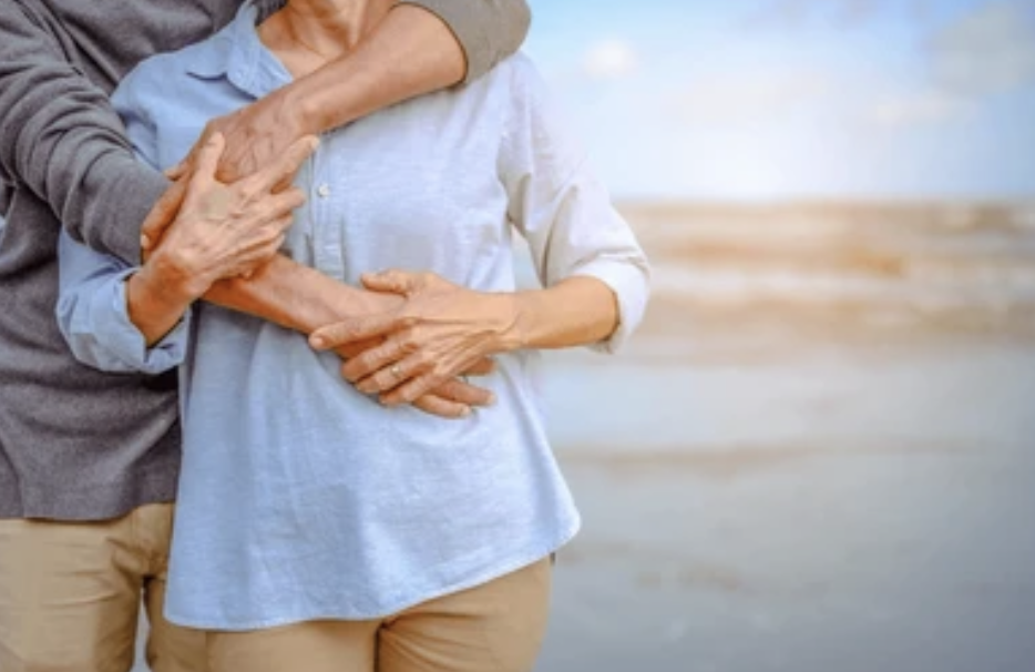 Close-up of elderly couple holding each other's hands on the beach.