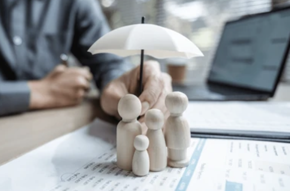 A person holding a small white umbrella over wooden figurines on a desk with documents and a laptop.