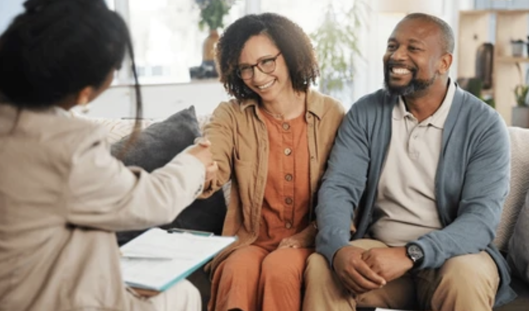 Therapist or counselor shaking hands with an attentive middle-aged couple during a therapy session in a cozy, well-lit office
