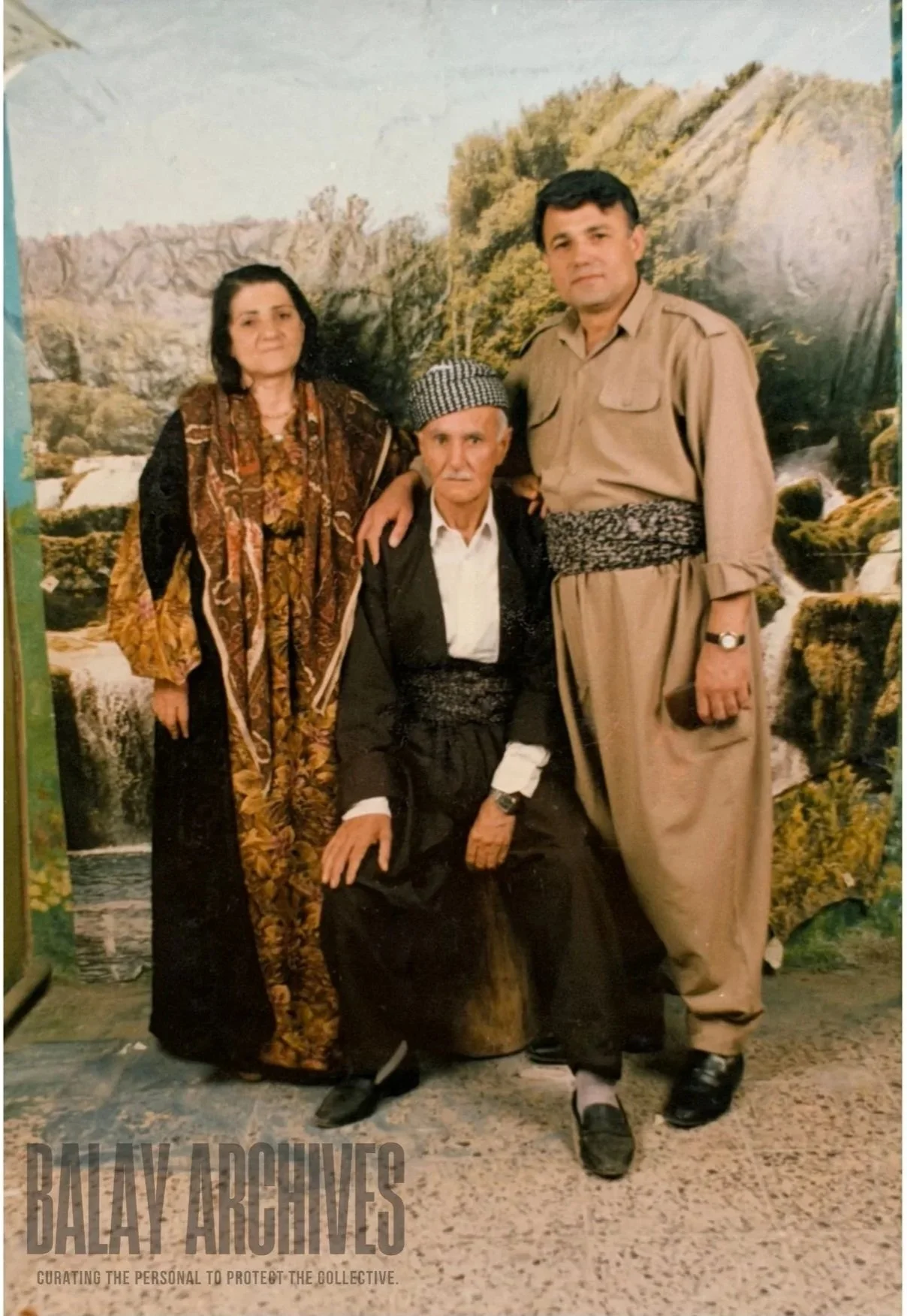 A family of four posing in traditional Kurdish attire, with a nature scene backdrop featuring mountains and a river.