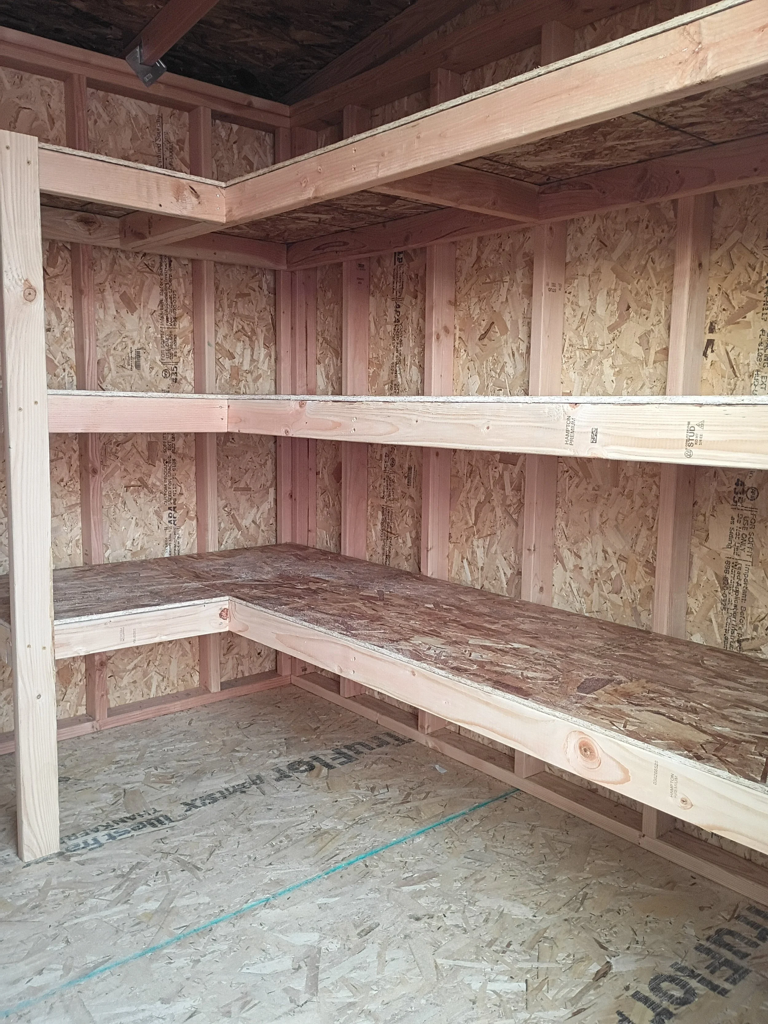 Empty unfinished wooden storage closet or shed with shelves and a floor, all made of particle board and plywood, with exposed framing and no hardware or doors.
