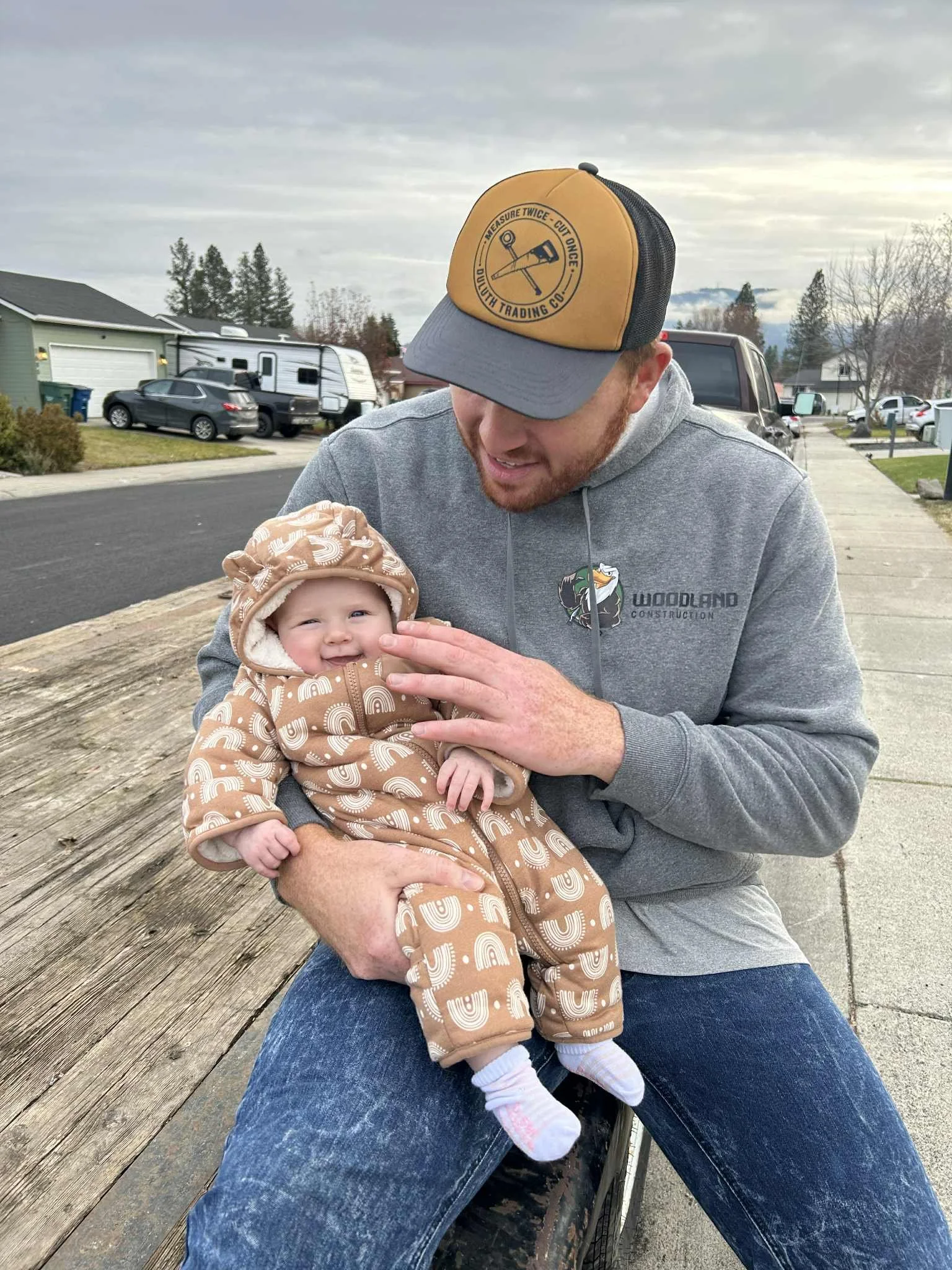 A man holding a smiling baby girl on a park bench in a residential neighborhood.