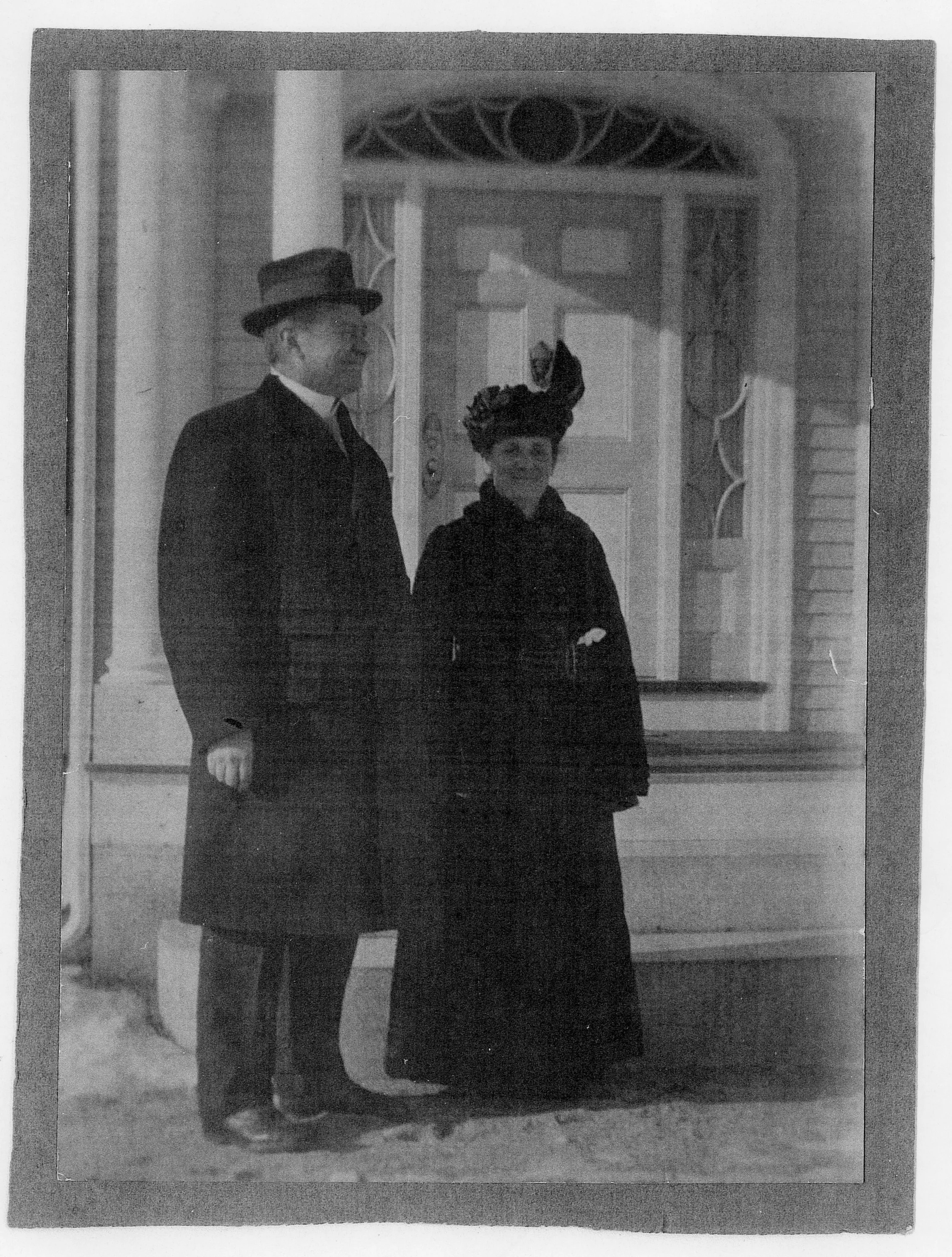 A man and woman dressed in vintage clothing standing outside a house with a decorative front door.