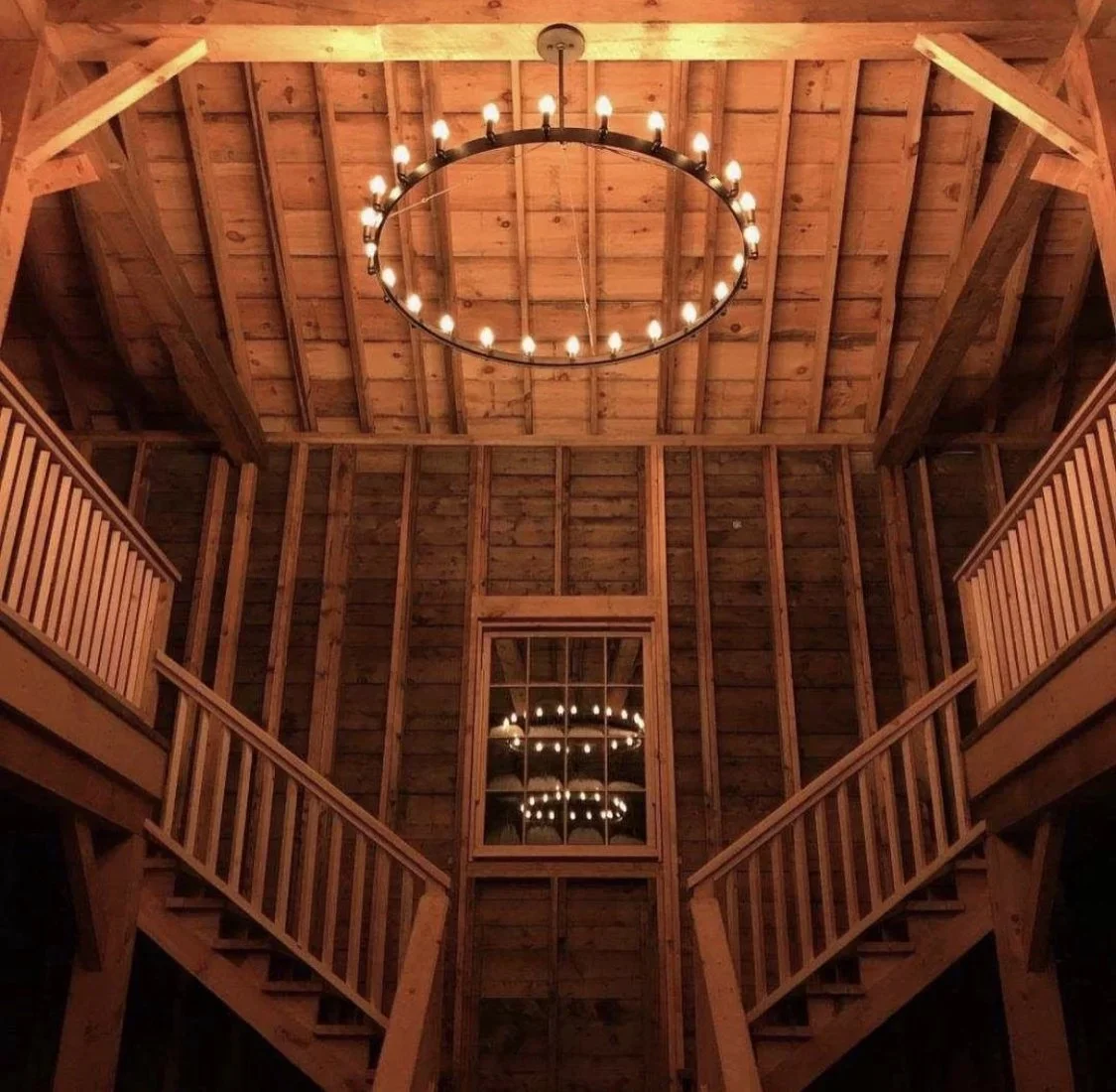 View of the interior of Wolf & Harp wedding estate with a high ceiling, a chandelier with multiple candle-like bulbs hanging from the ceiling, and a mirror reflecting the chandelier