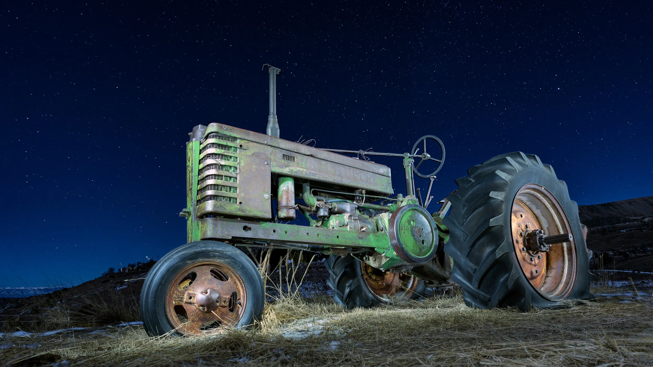 Old green tractor on dry grass at night with a starry sky.
