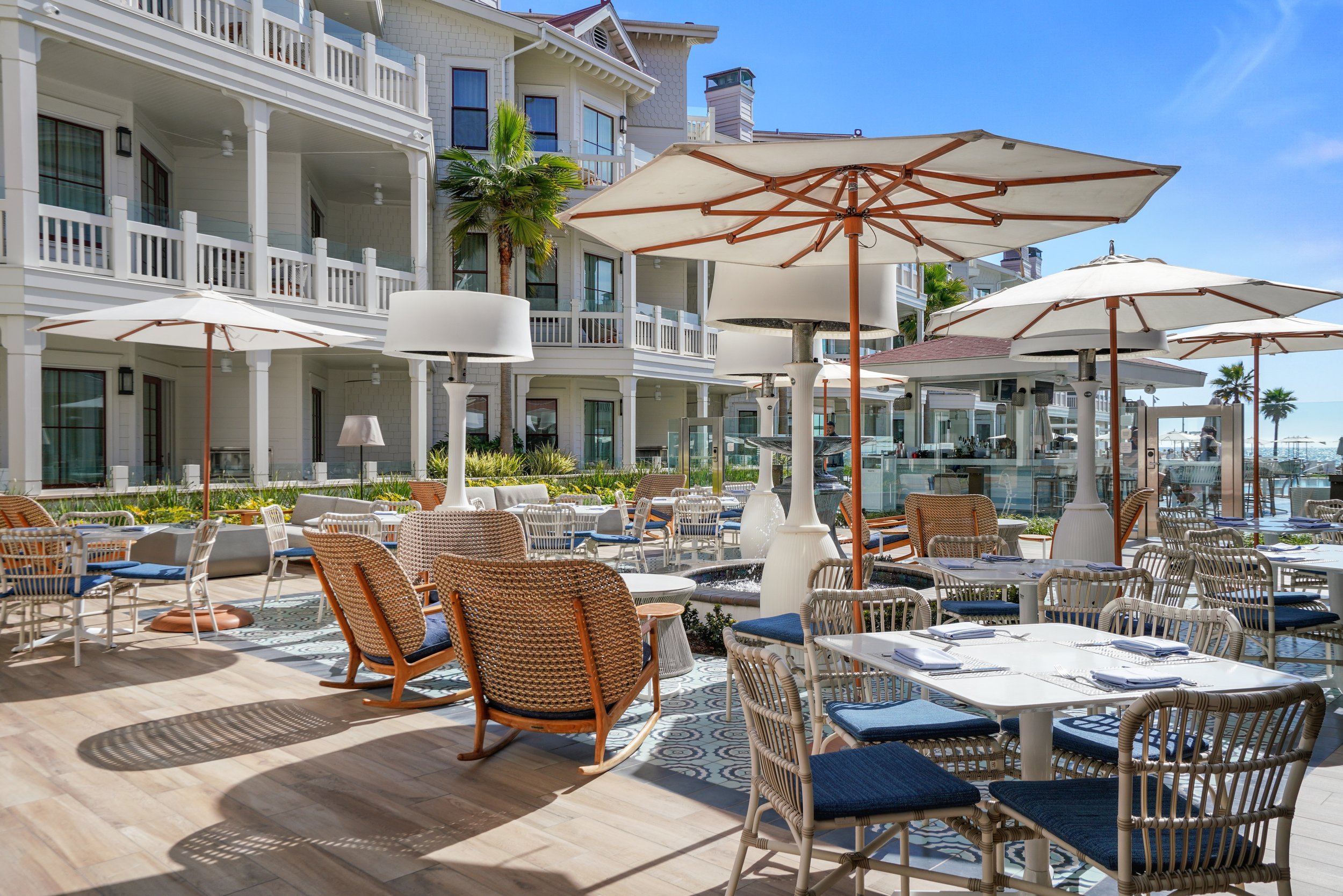 Outdoor restaurant patio at Hotel Del Coronado with white tables, blue cushioned chairs, umbrellas.