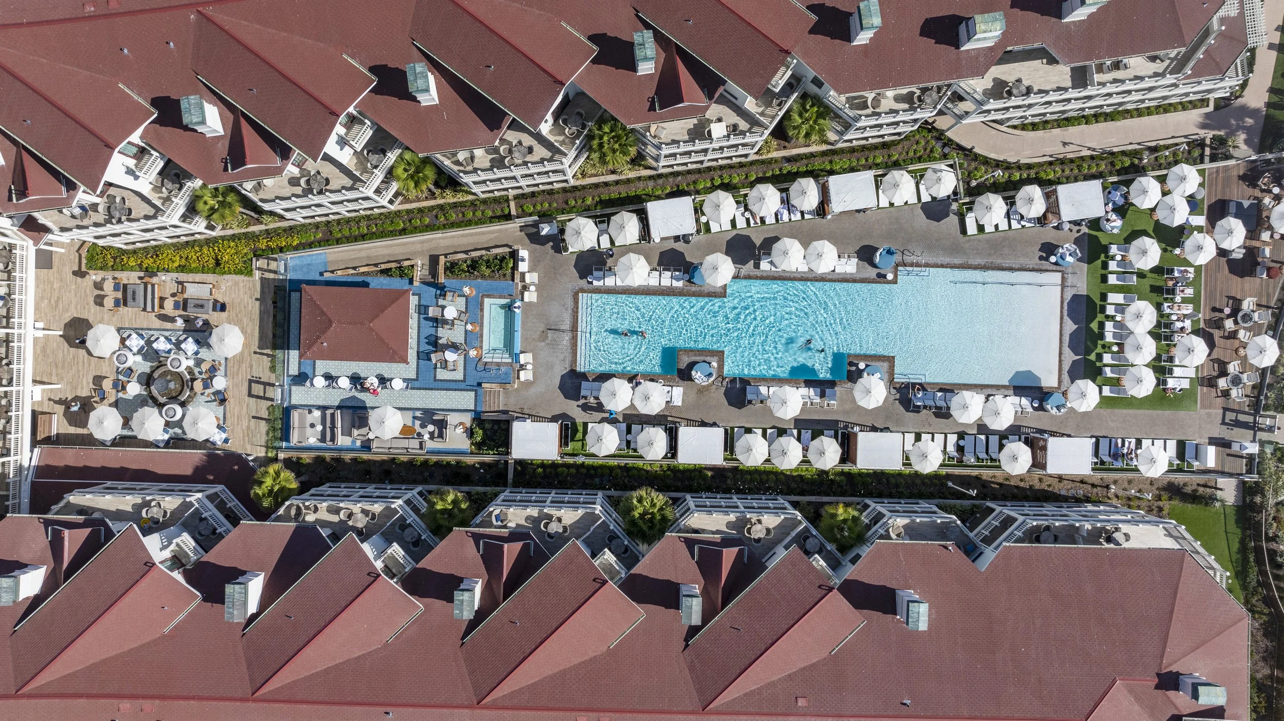 Drone photo of Hotel Del Coronado pool area surrounded by lounge chairs and umbrellas.