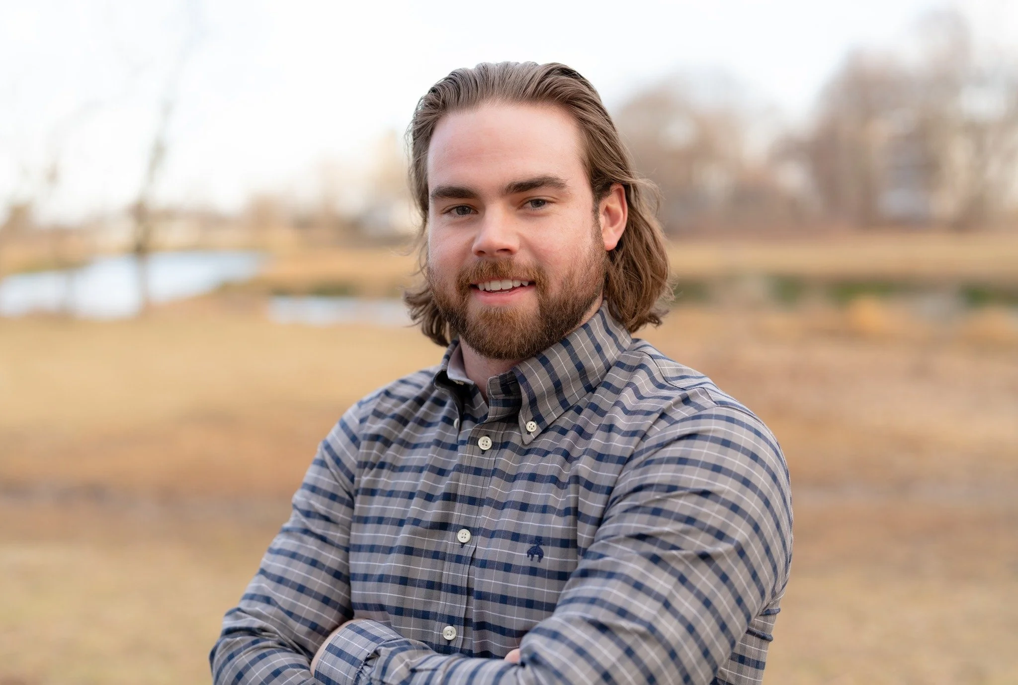 Pat Garrigan wearing a plaid button-up shirt, smiling with arms crossed outdoors in Boston.