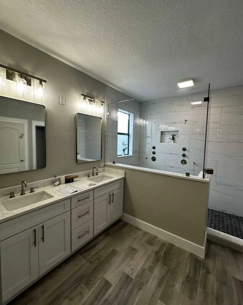 Bathroom with a double vanity, two mirrors, and separate shower area with white tiled walls, window, and small potted plant.