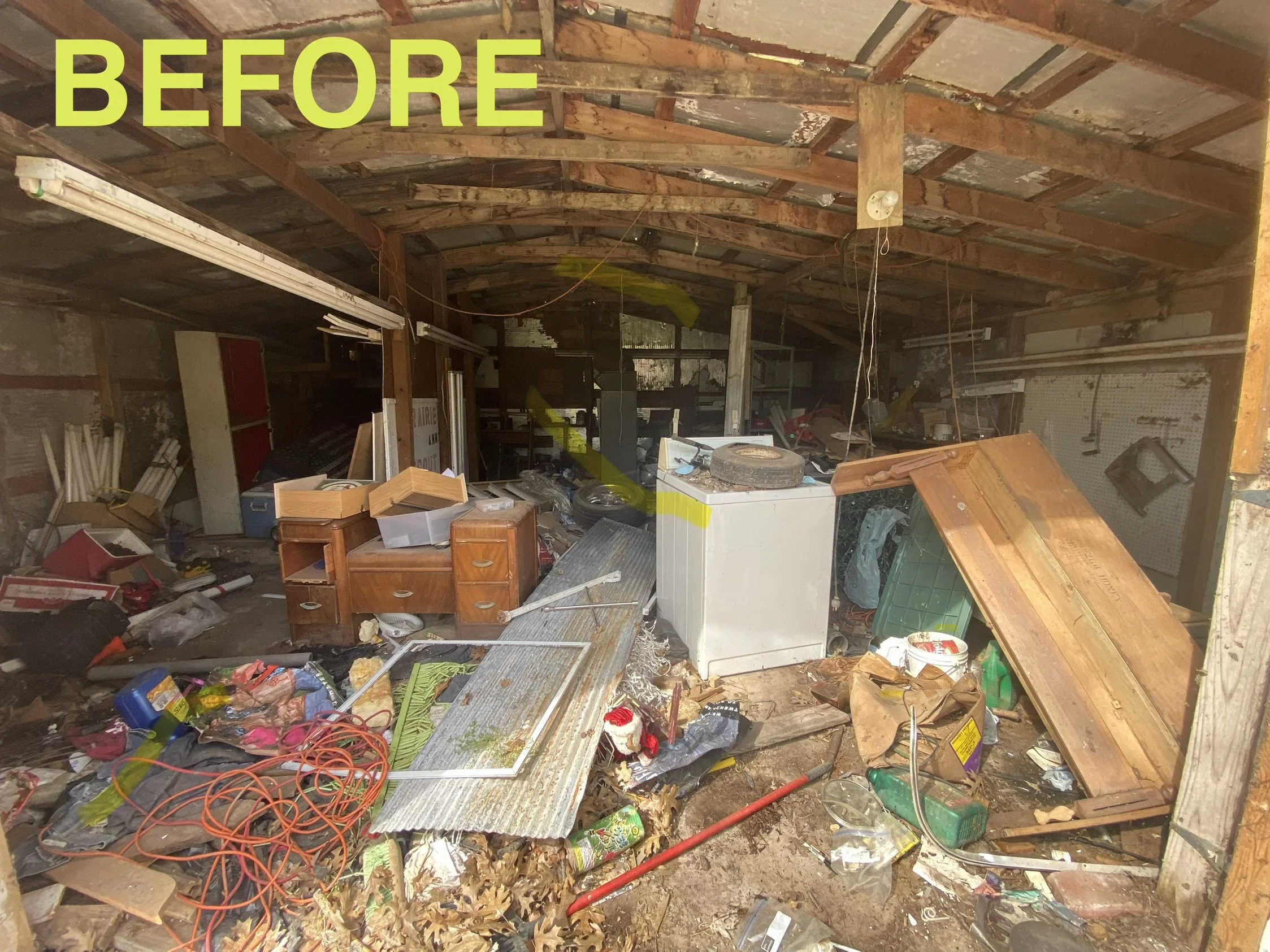 Cluttered and messy basement or storage room with scattered items including furniture, cables, tools, and debris, with a wooden ceiling and wall.