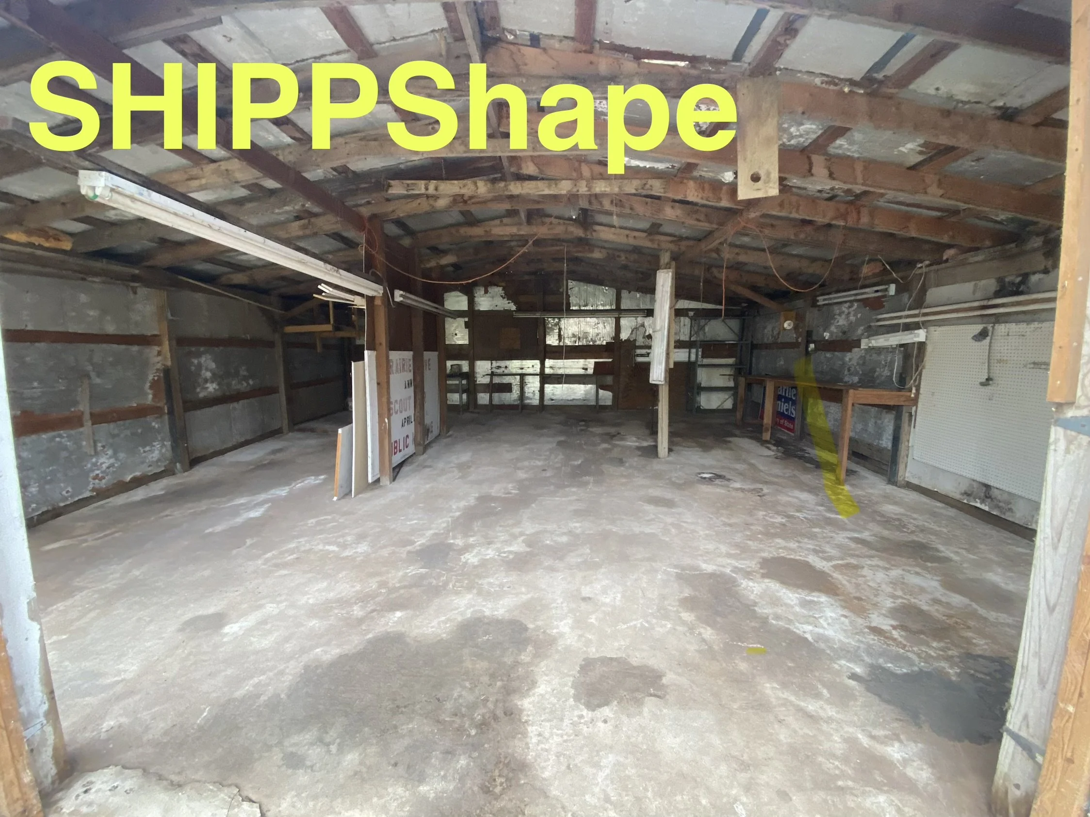 Empty garage with unfinished walls and exposed wooden beams, with the word 'SHIPPShape' overlaid in large yellow text.