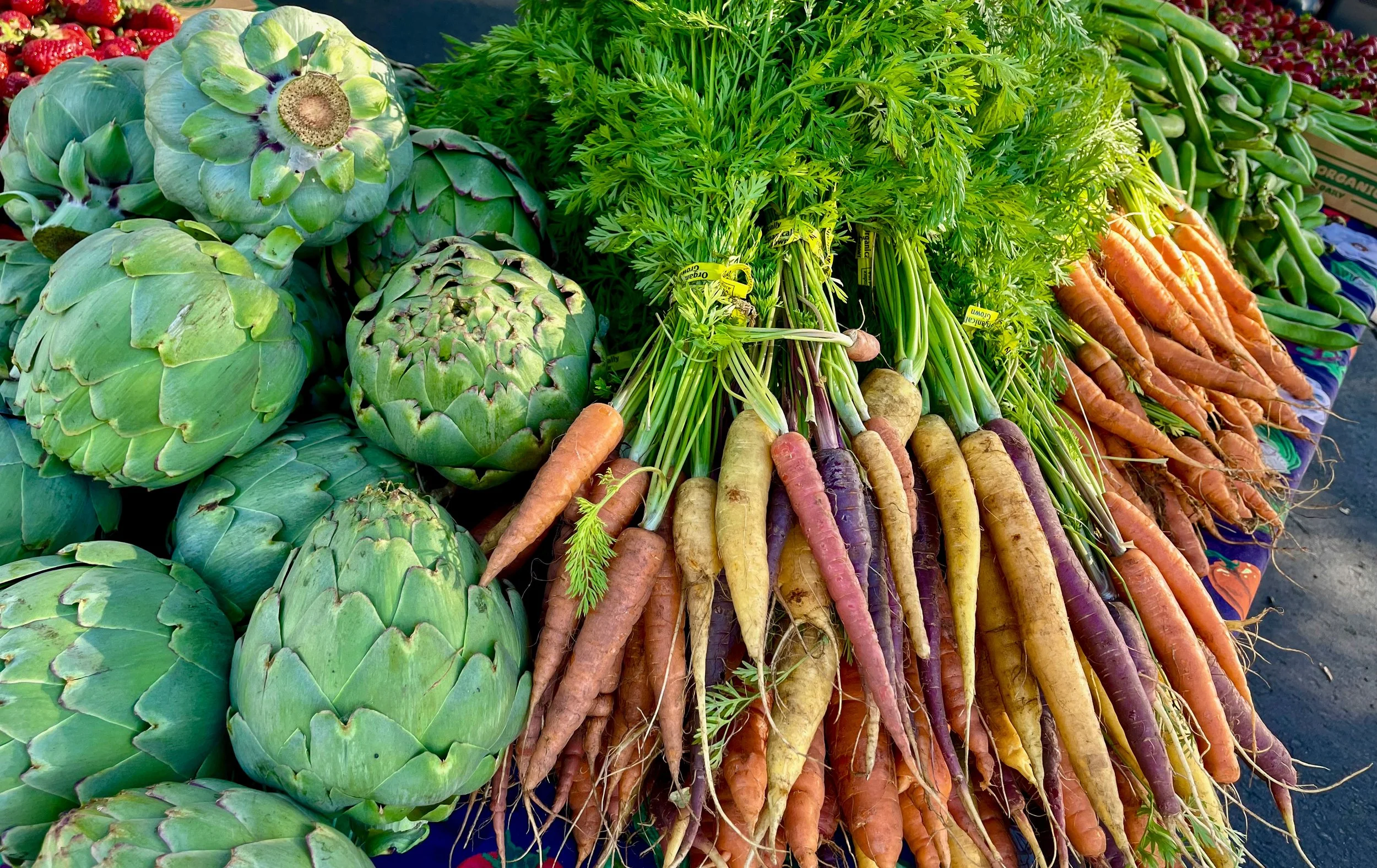 Fresh artichokes and a variety of multi-colored carrots displayed at a farmers market