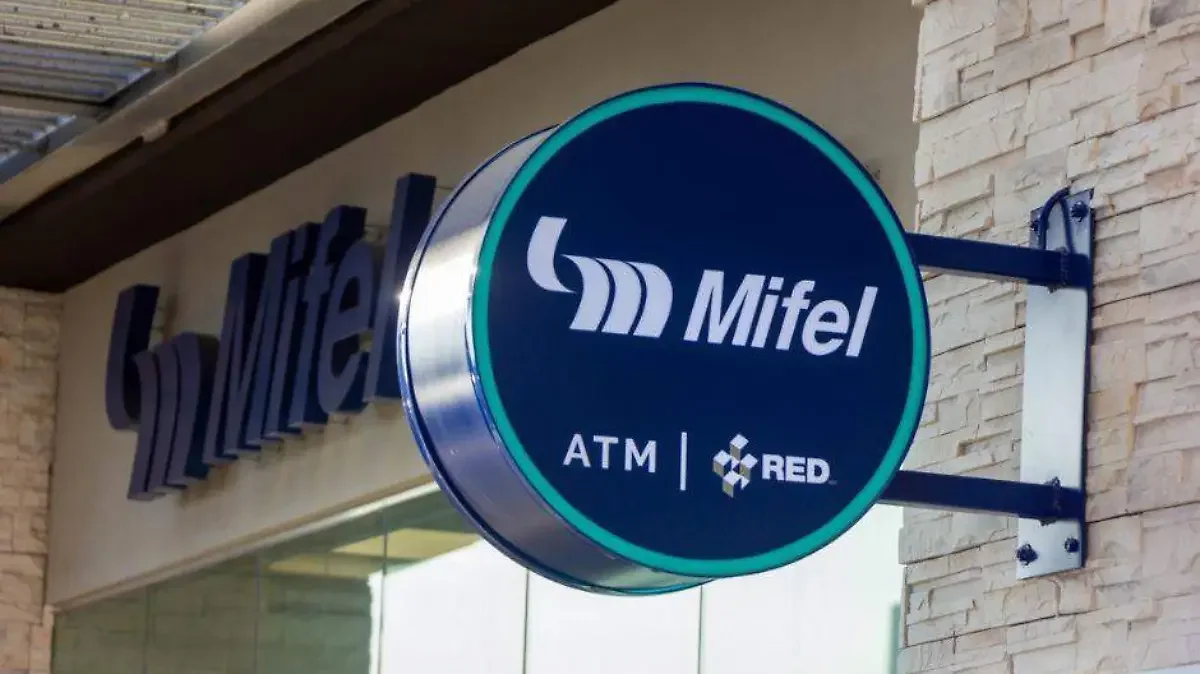 Sello con logotipo de Mifel, banco, ATM, y la marca RED en un cartel redondo azul oscuro con borde celeste, instalado en la pared de un edificio.