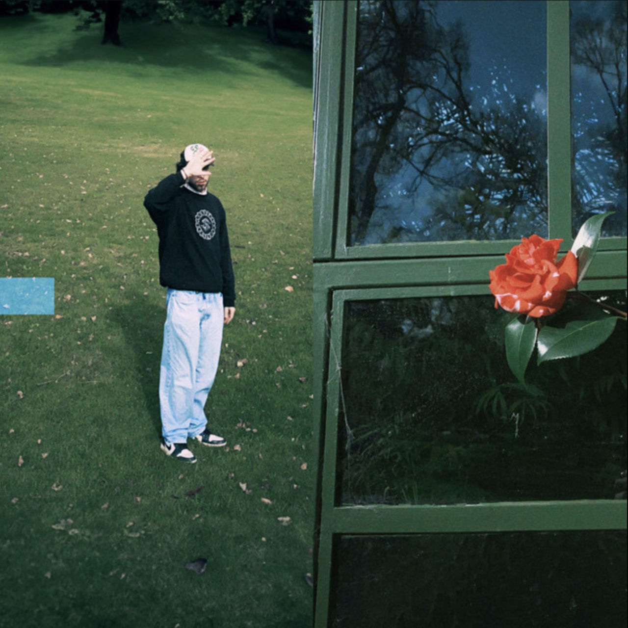 A hand with a tattooed wrist shielding the eyes of a man standing on grass in a park. The image is split with part showing the park and the man, and part showing a window with a reflection of trees and a red flower. SwimGood